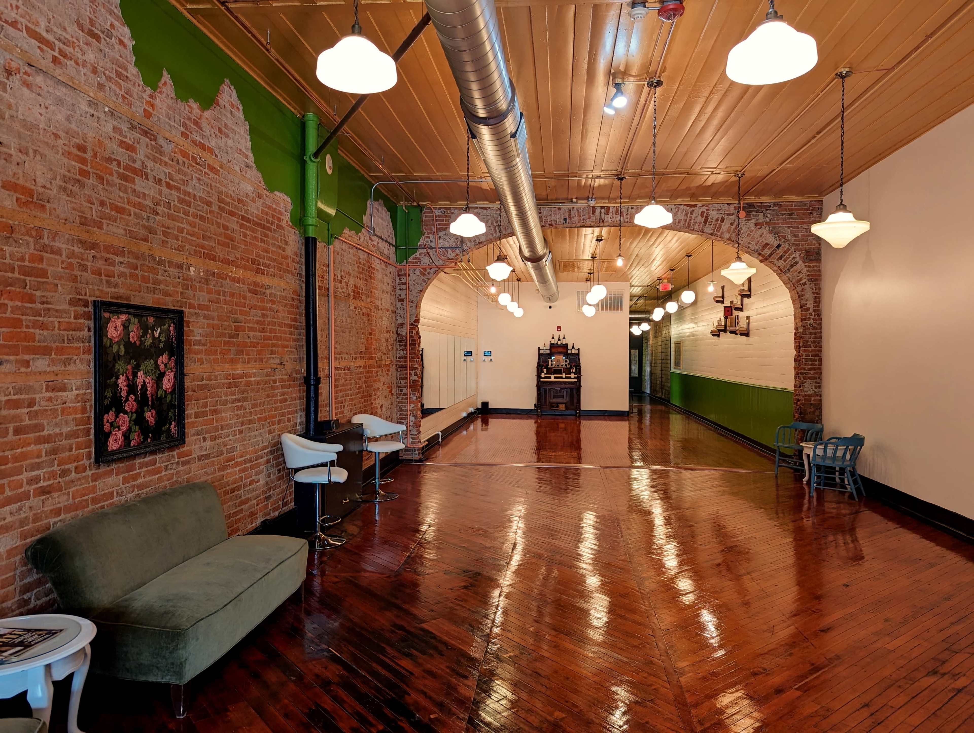 An interior space with exposed brick walls, polished wooden floors, and several hanging light fixtures.