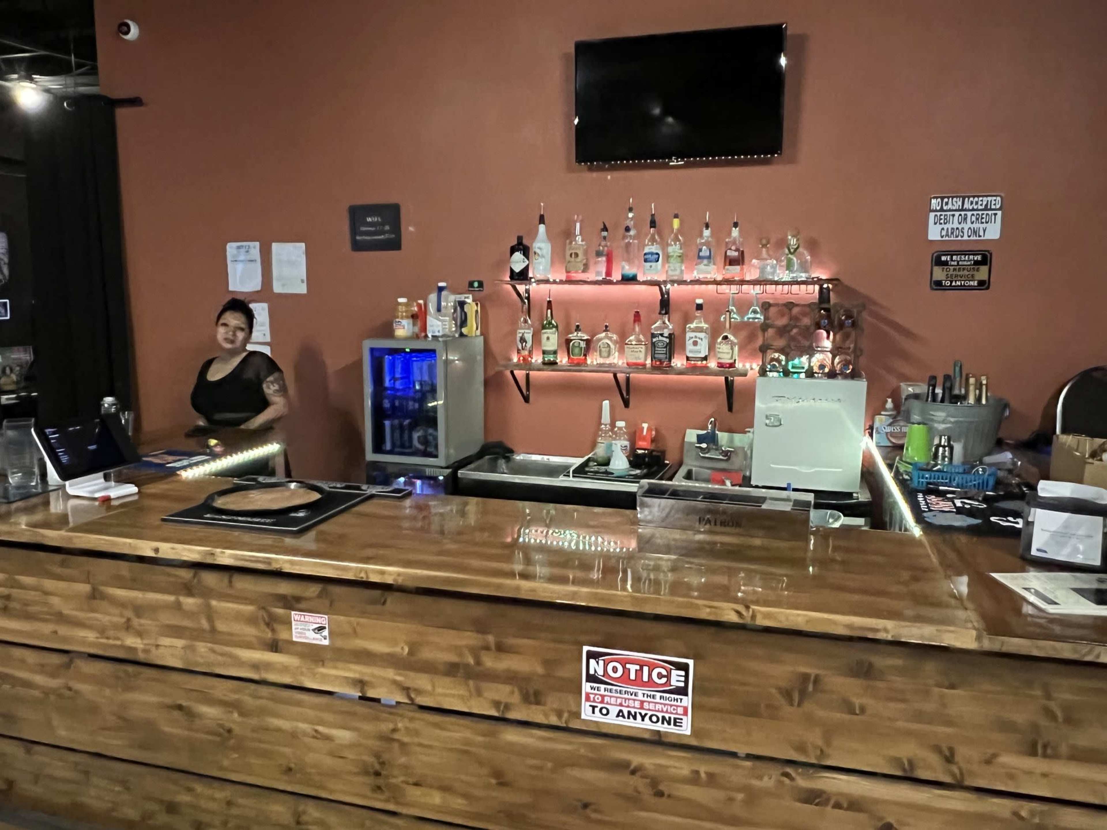 A wooden bar with various liquor bottles displayed on shelves behind it and a server standing nearby.