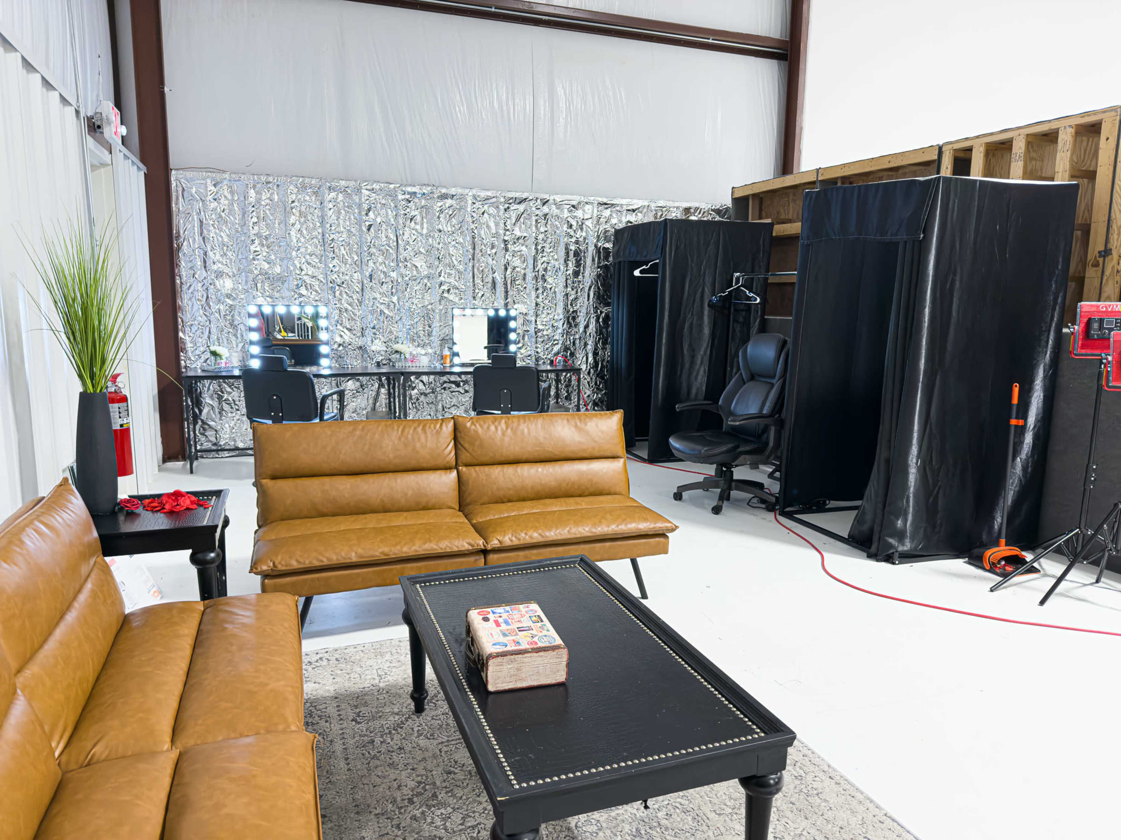 The image shows a modern studio space with brown leather sofas, a coffee table, and a backdrop area featuring black partitions and a desk with illuminated mirrors.
