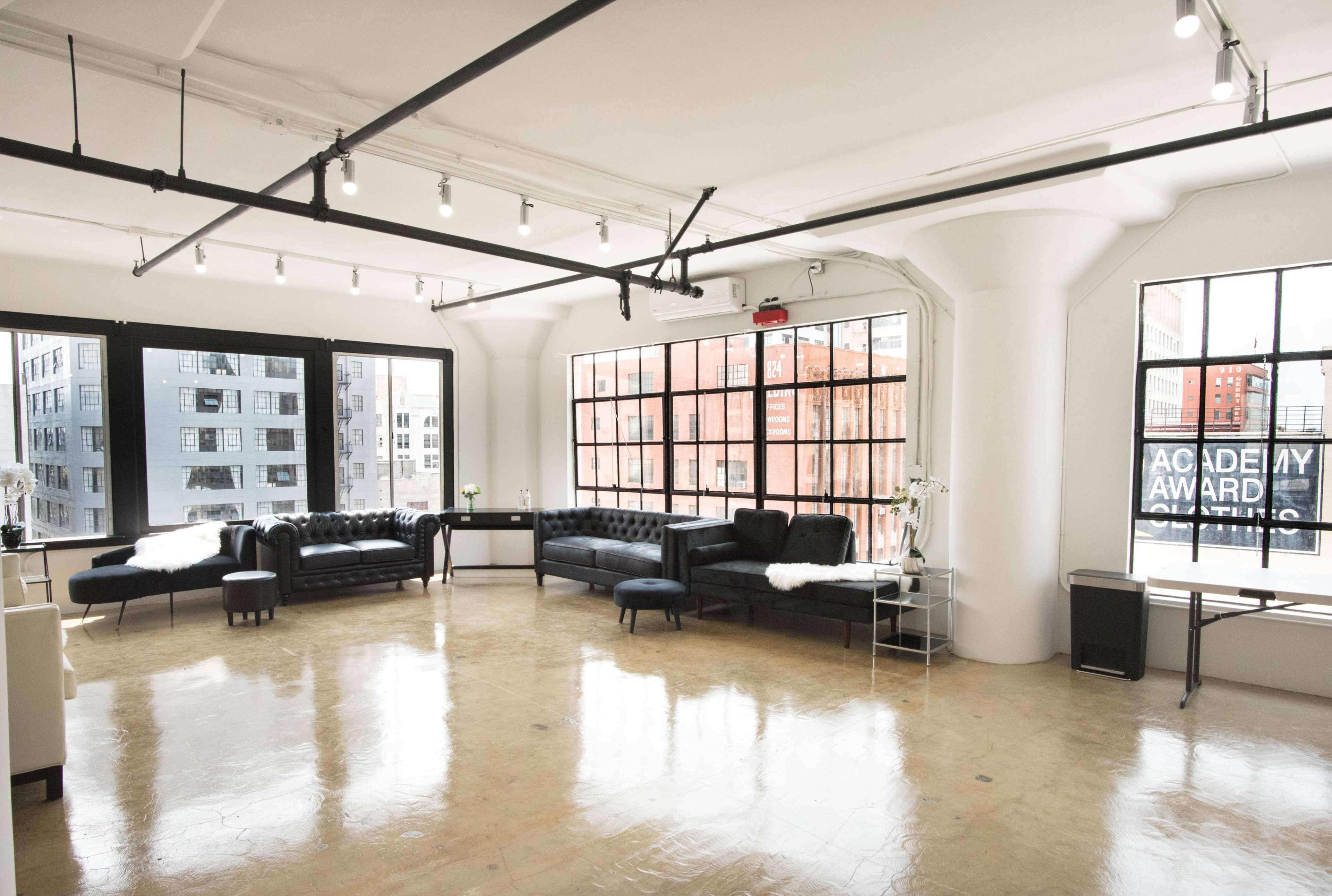 A spacious, well-lit interior features black sofas and large windows with city views.