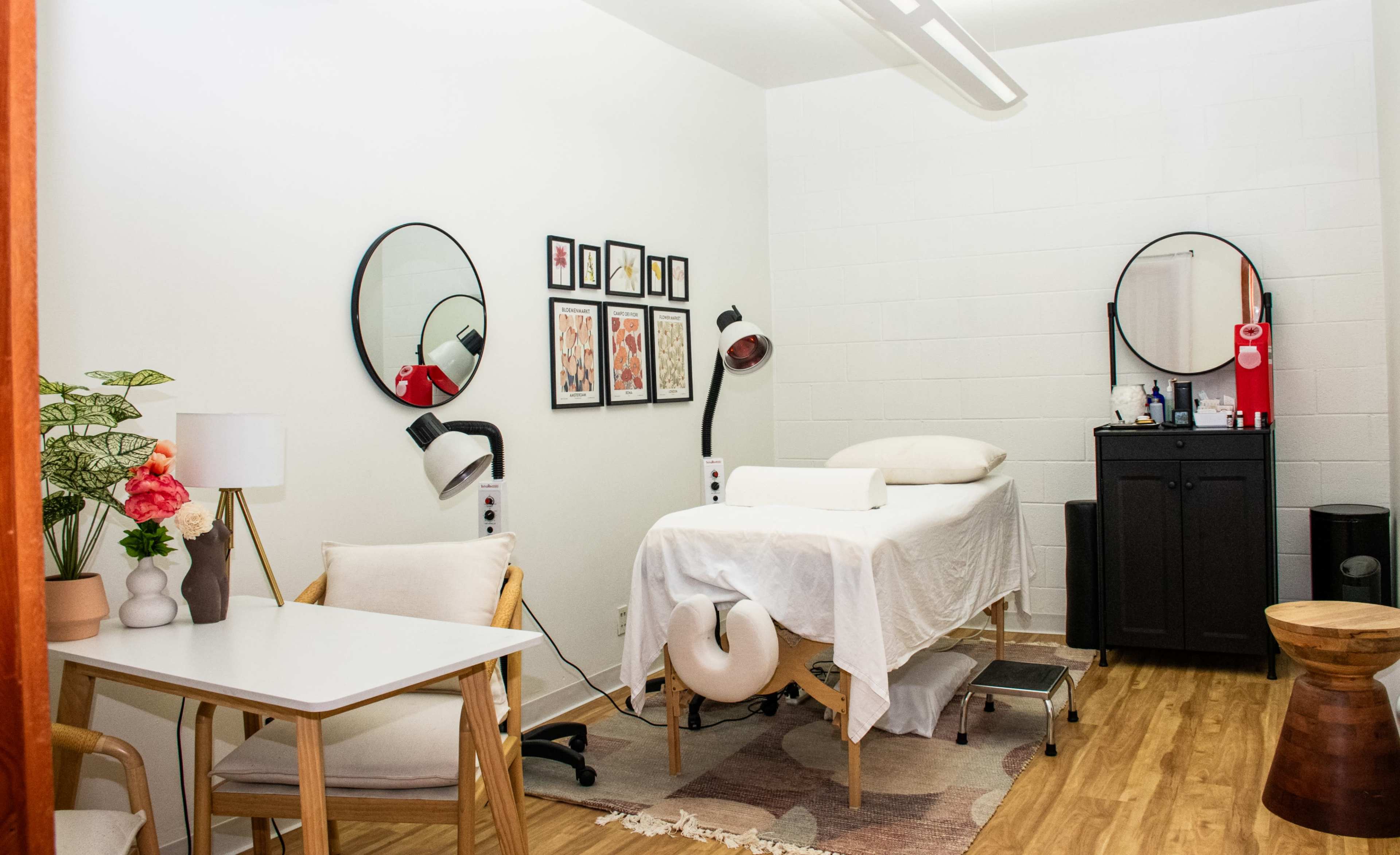 A small treatment room features a massage table, a desk, two mirrors, and various decorations on the walls.