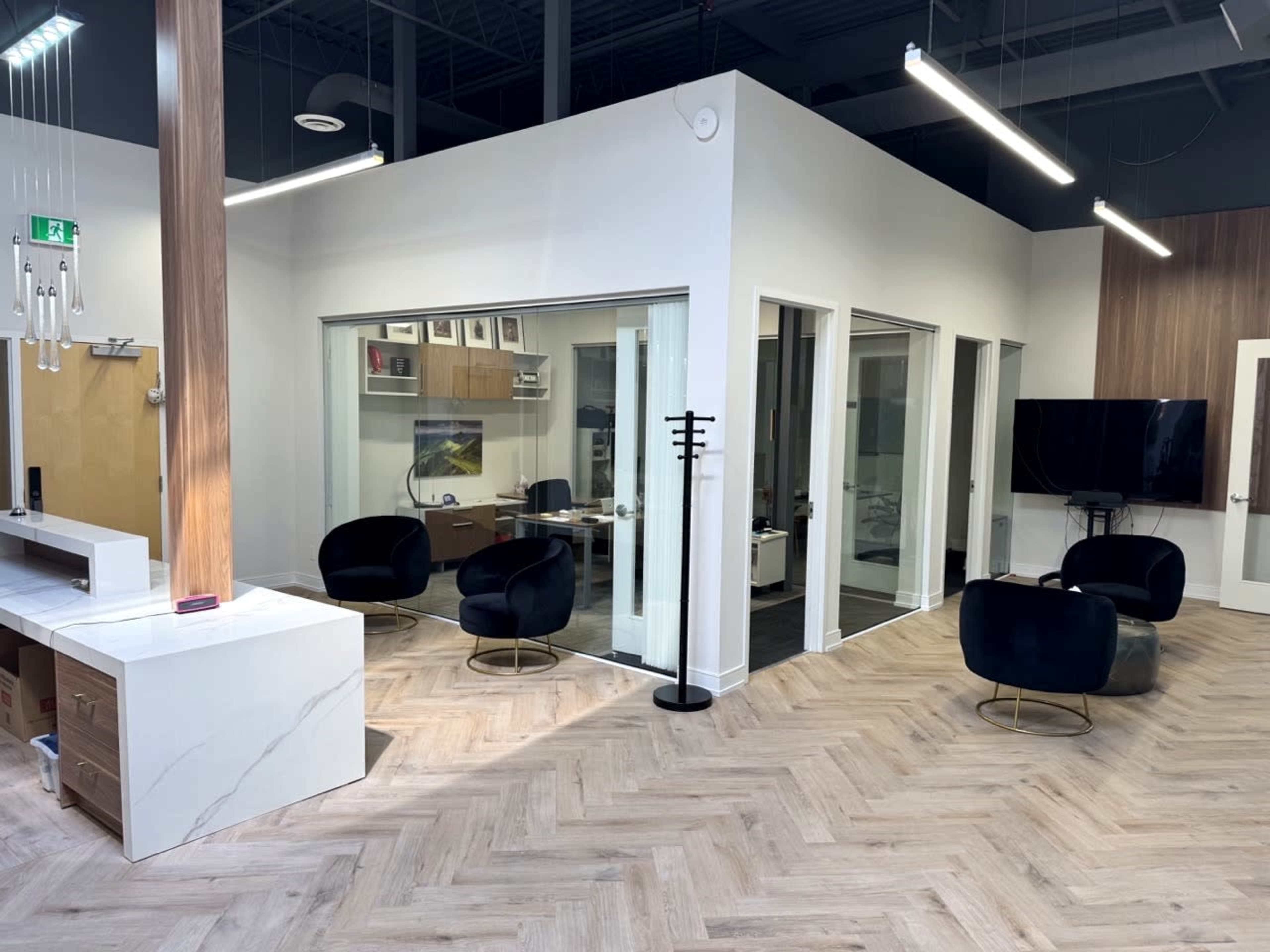 The image shows a modern office space with glass-walled meeting rooms, black chairs, and a wooden accent wall.
