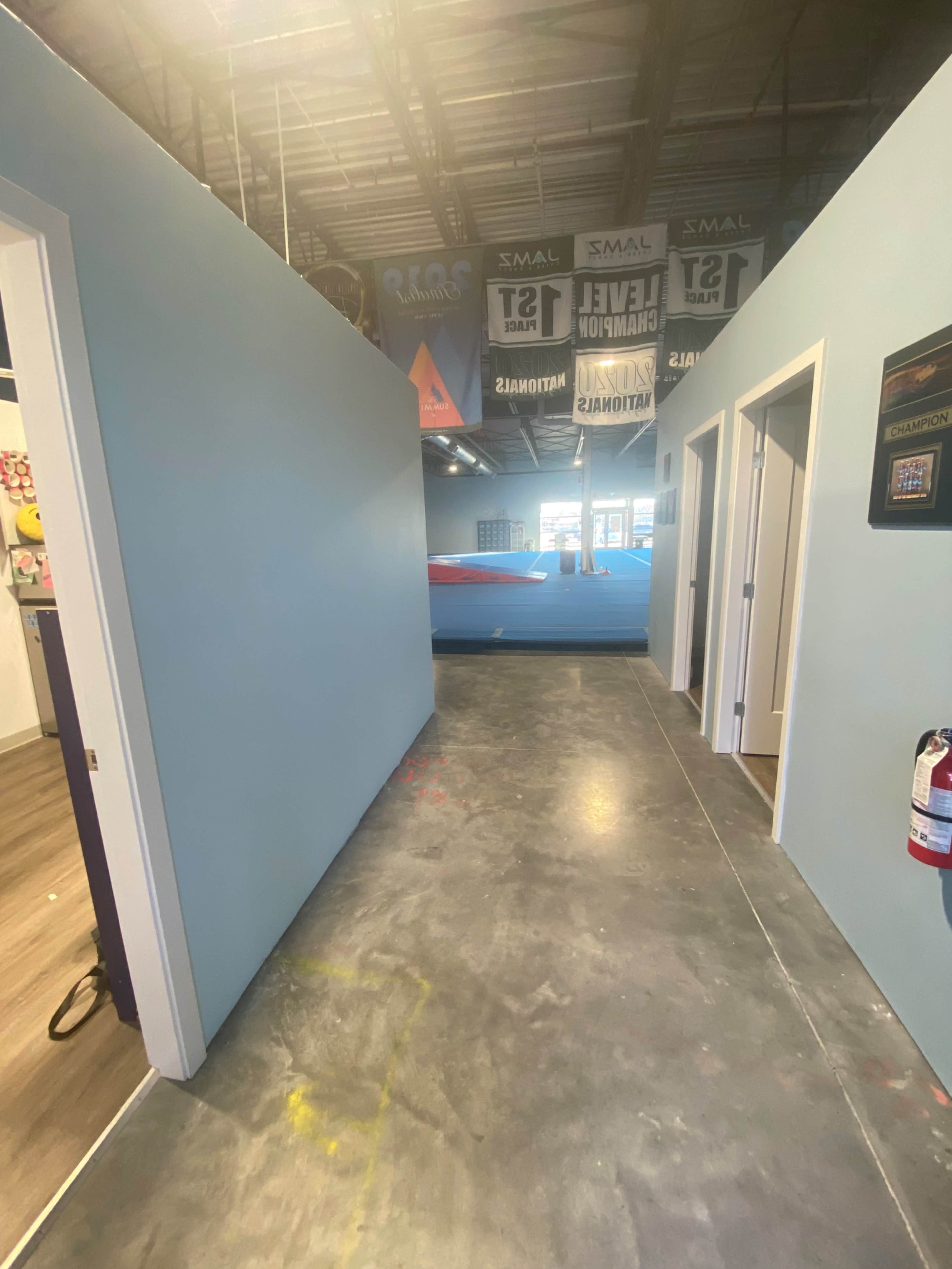A hallway in a building with light blue walls, leading towards an area with a large blue obstacle or equipment visible at the end.