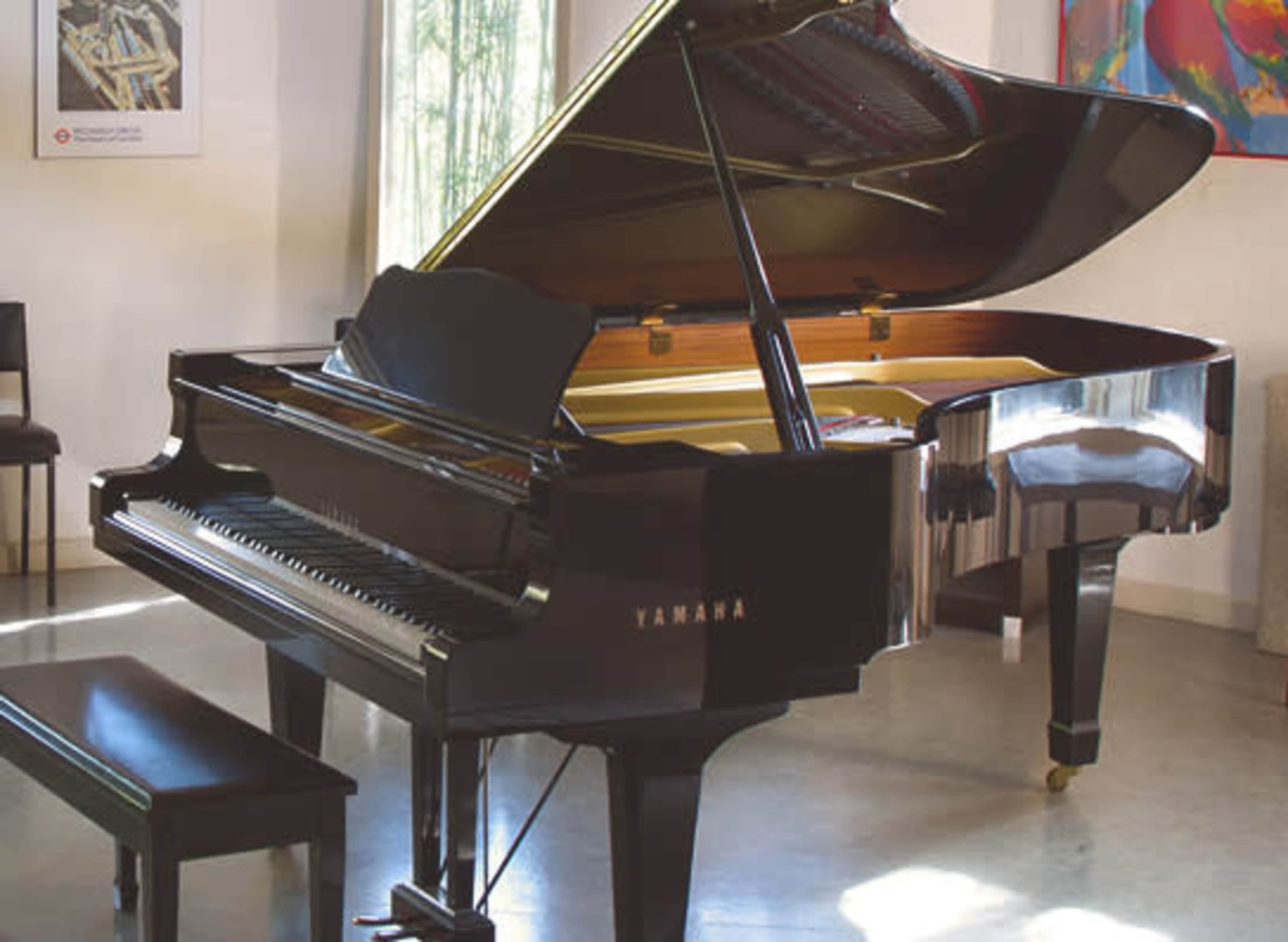 A black Yamaha grand piano is positioned in a well-lit room with large windows and minimalist decor.