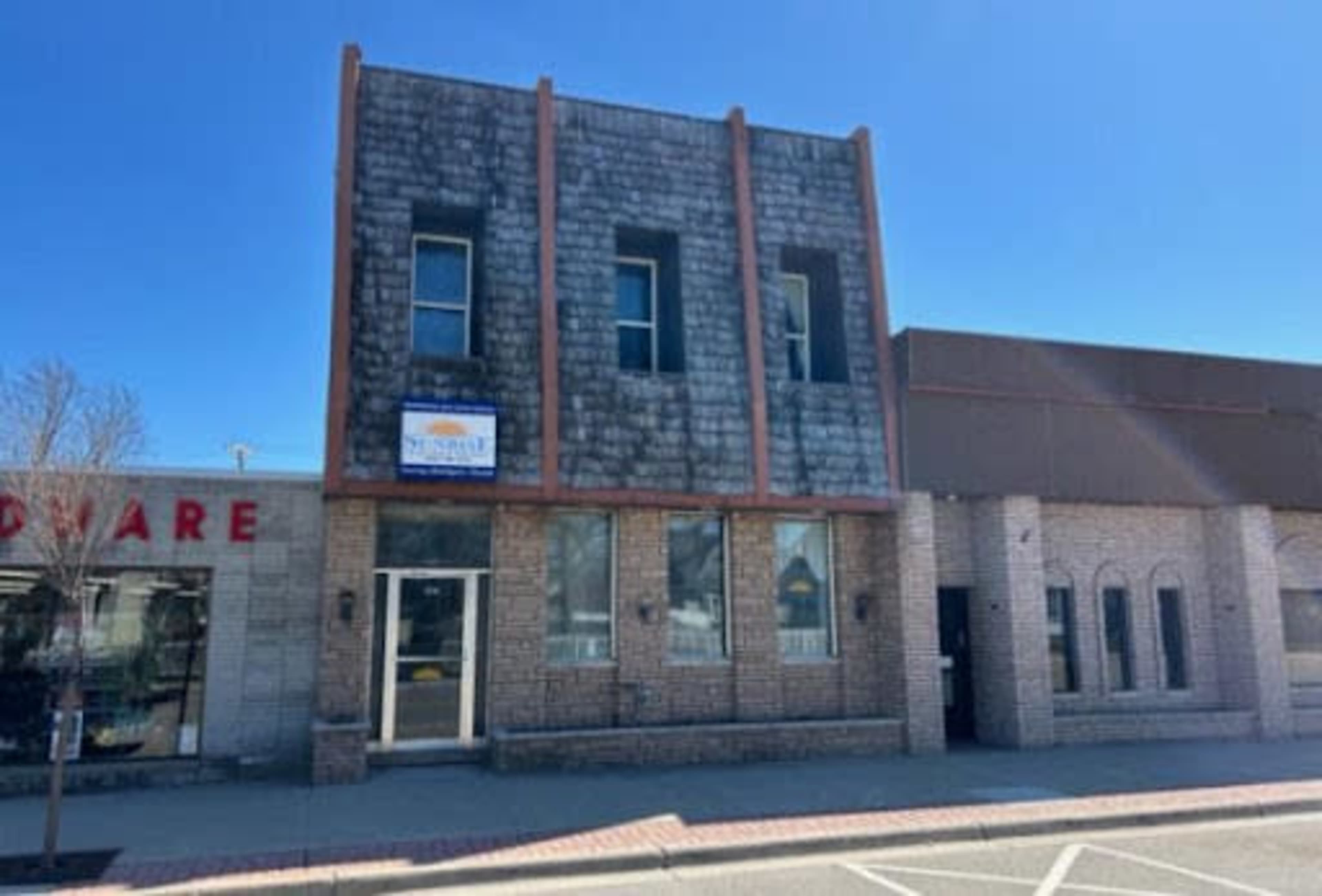 The image shows a two-story brick building with a stucco facade, adjacent to a hardware store.
