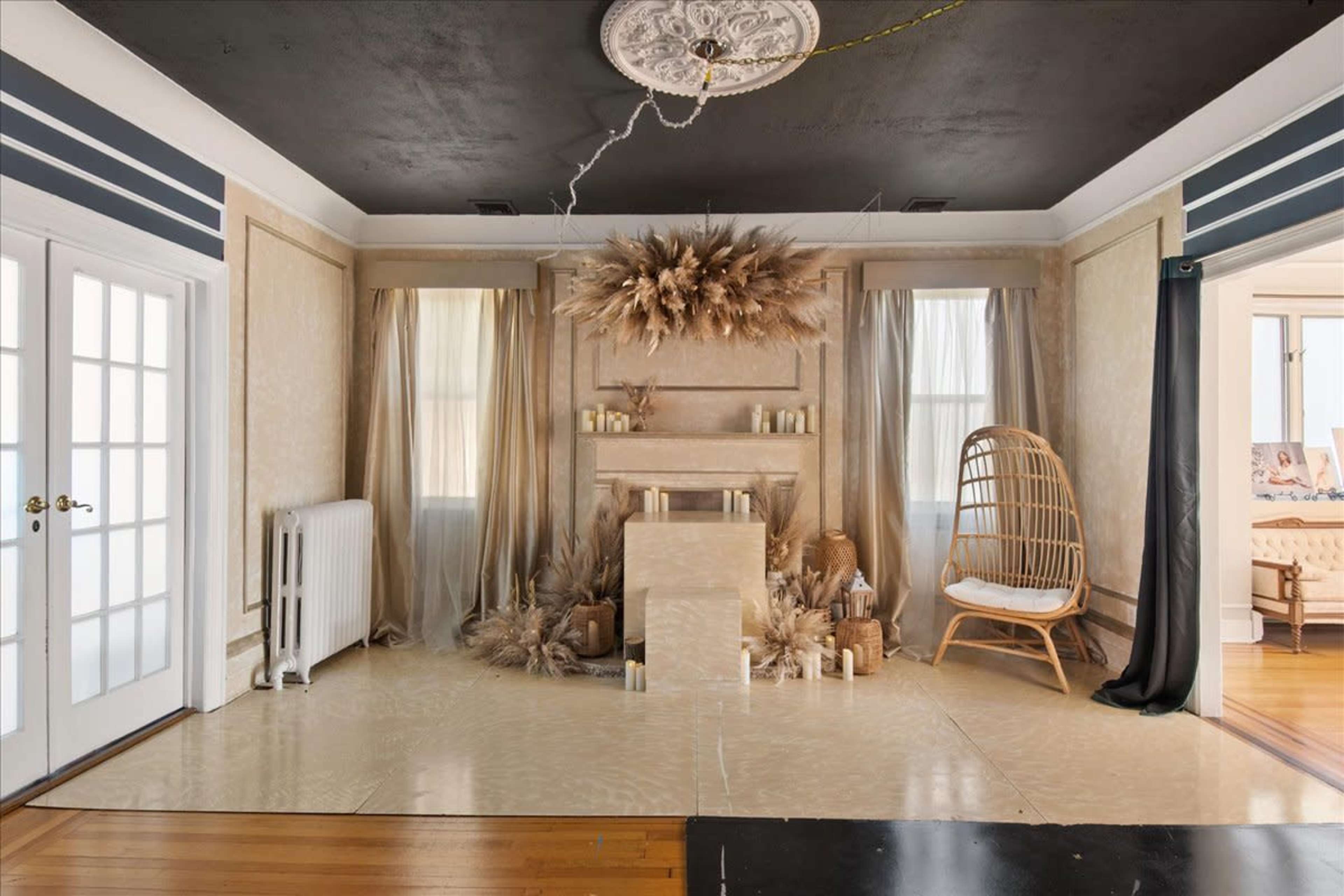 The interior features a decorated wall with a fireplace, surrounded by fabric drapes, candles, and a rattan chair in a spacious room.