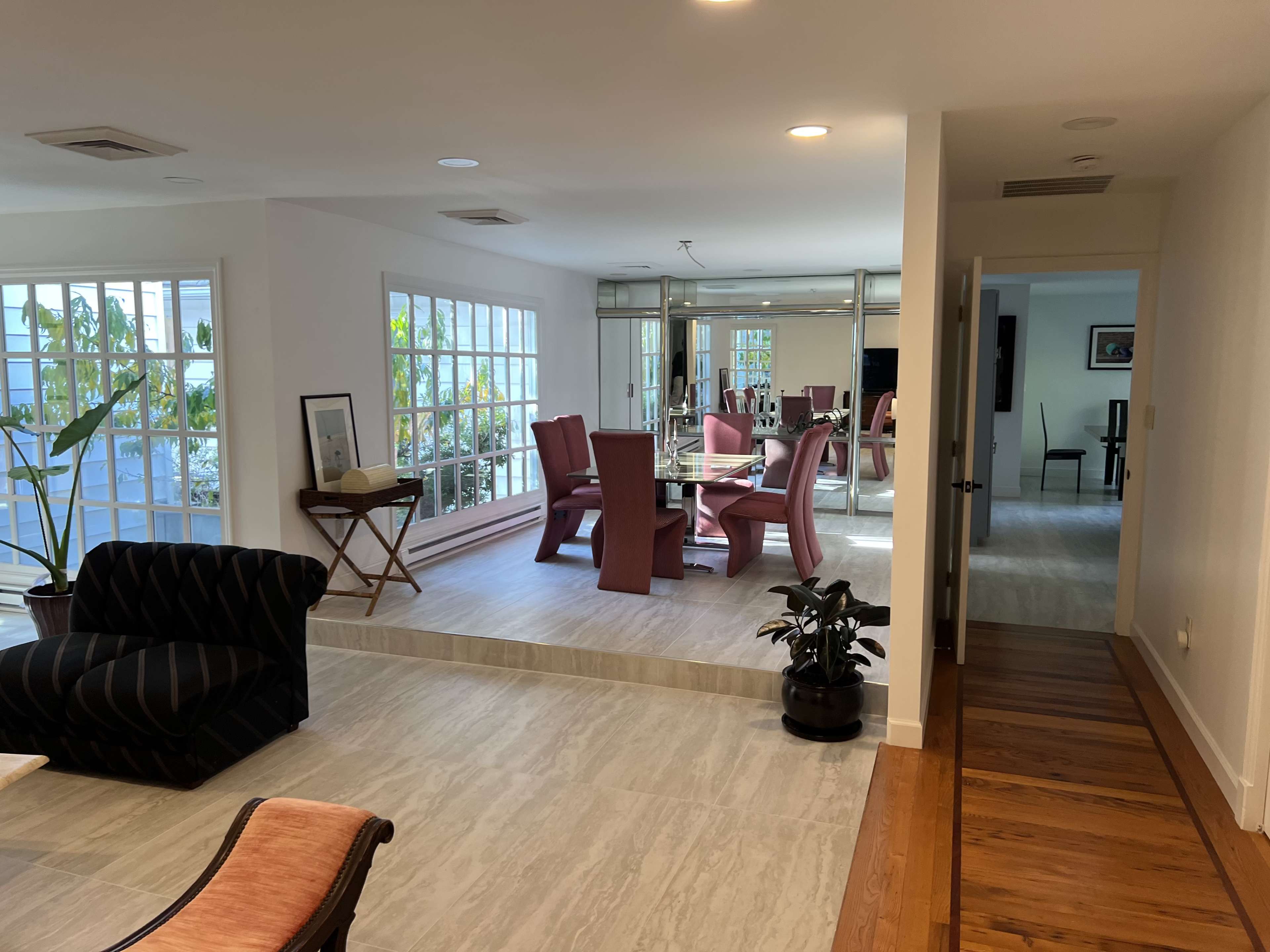 A modern living space with a view of a dining area featuring a glass table and red chairs, separated by a level change.