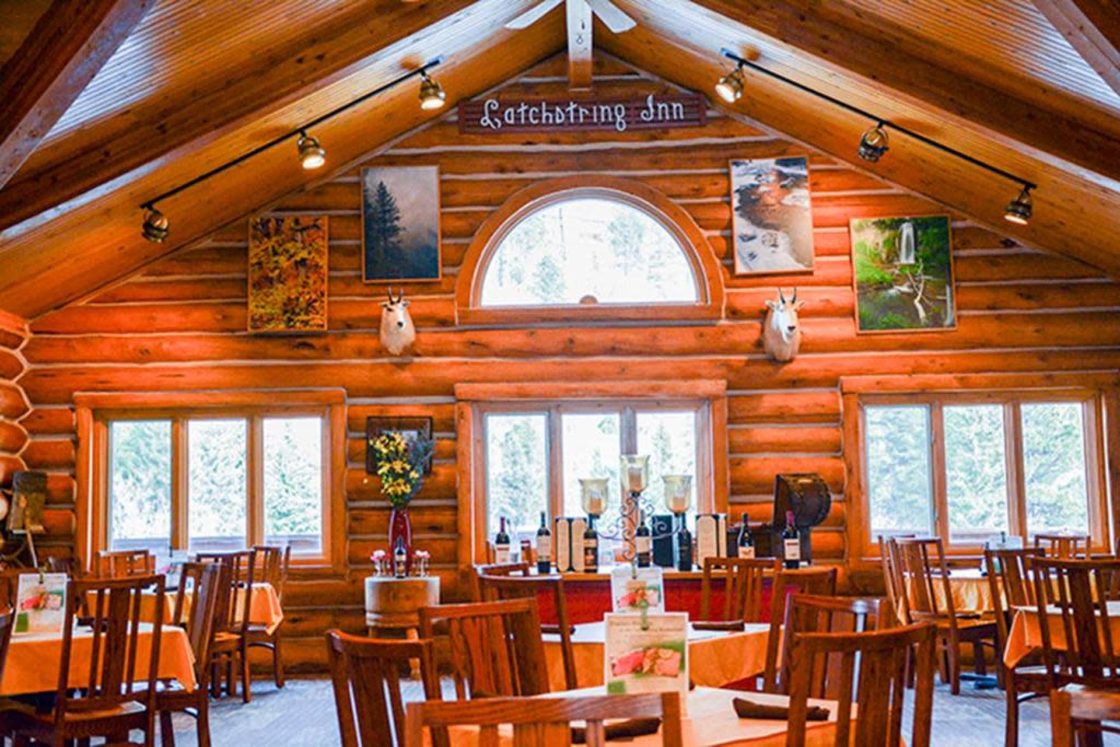 The image shows a rustic restaurant interior with wooden walls, several tables, framed artwork, and large windows providing natural light.