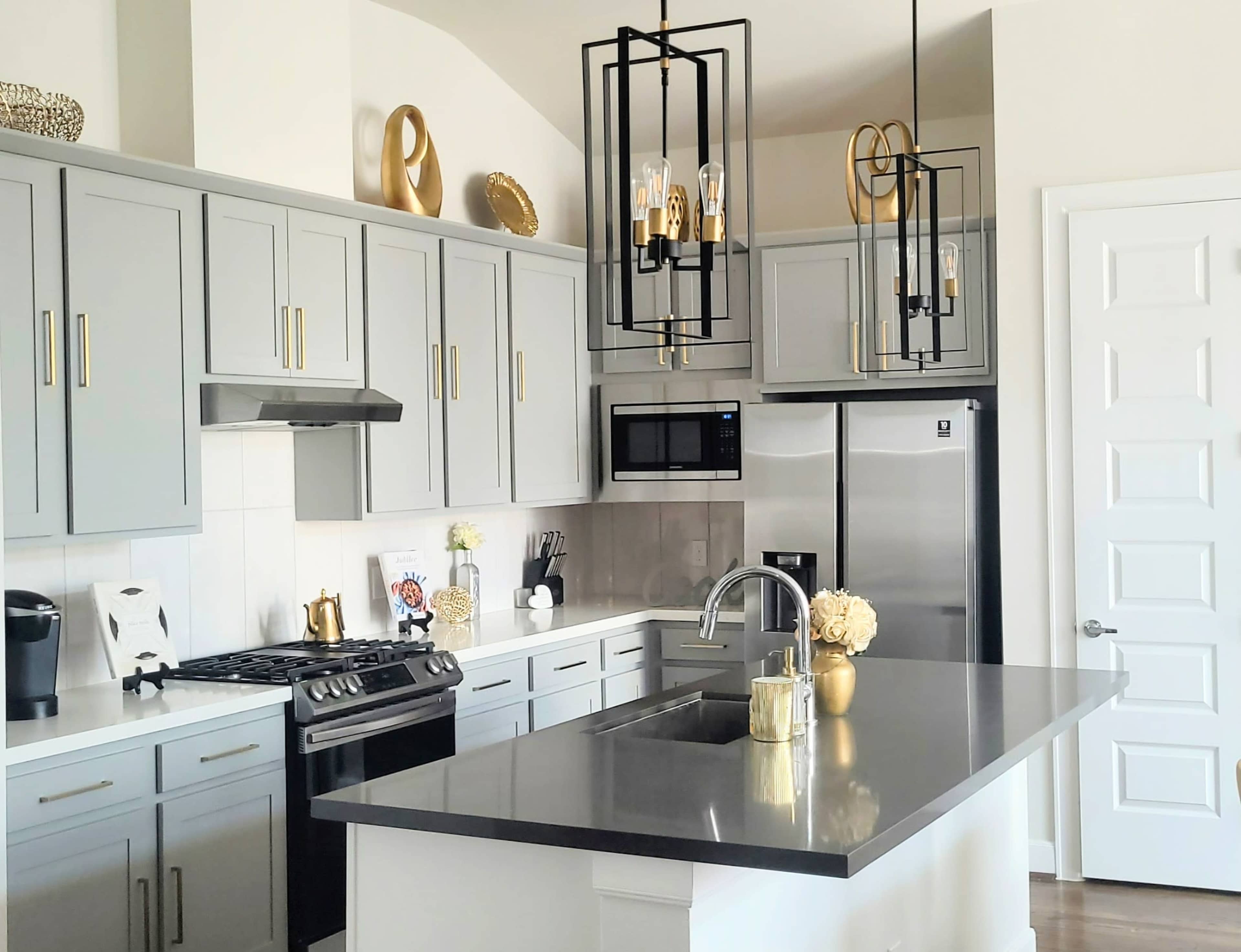 A modern kitchen featuring gray cabinets, stainless steel appliances, a center island with a dark countertop, and pendant lighting overhead.