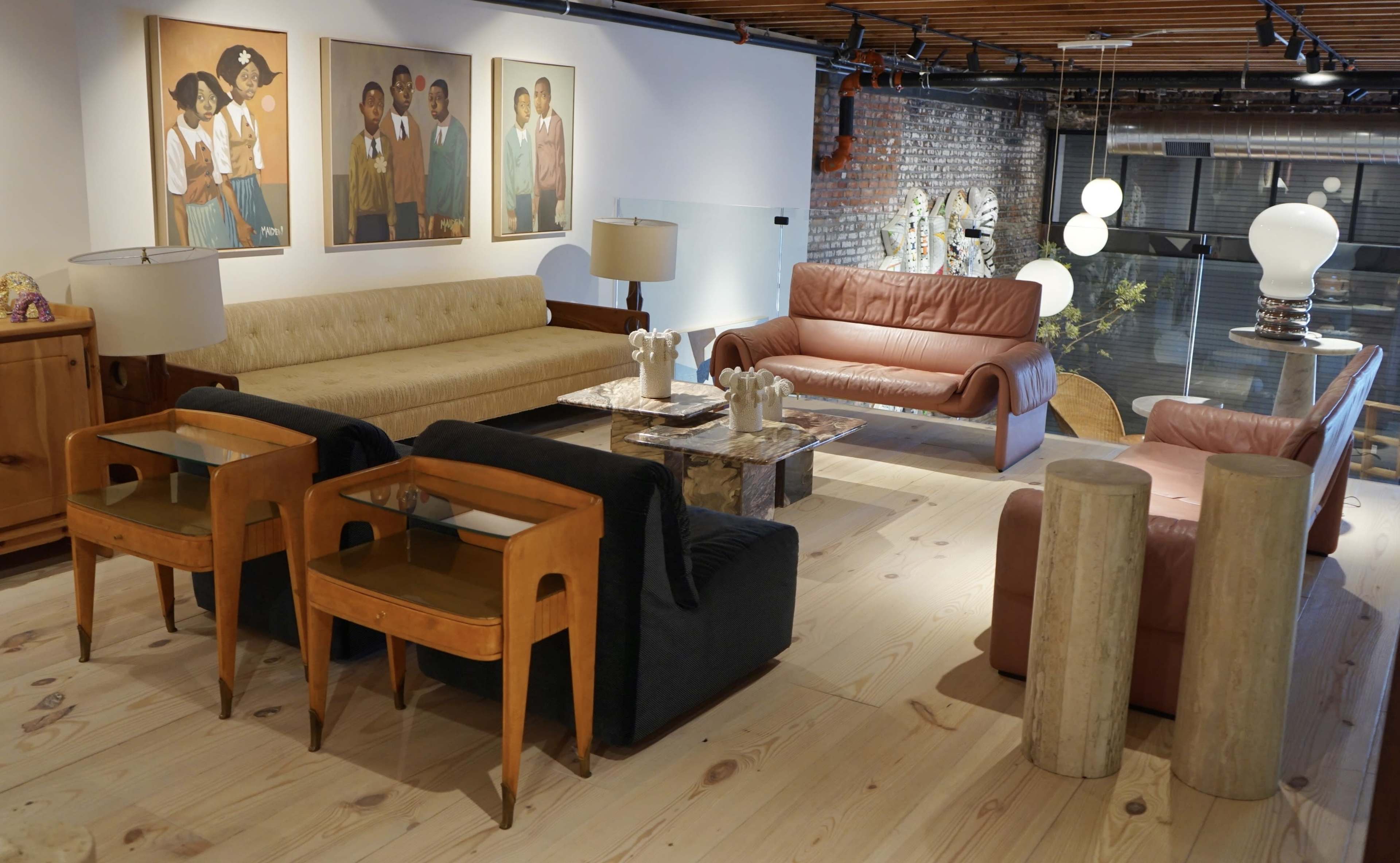 A cozy lounge area featuring a mix of modern and vintage furniture, including sofas, chairs, and a coffee table, alongside artwork on the walls.