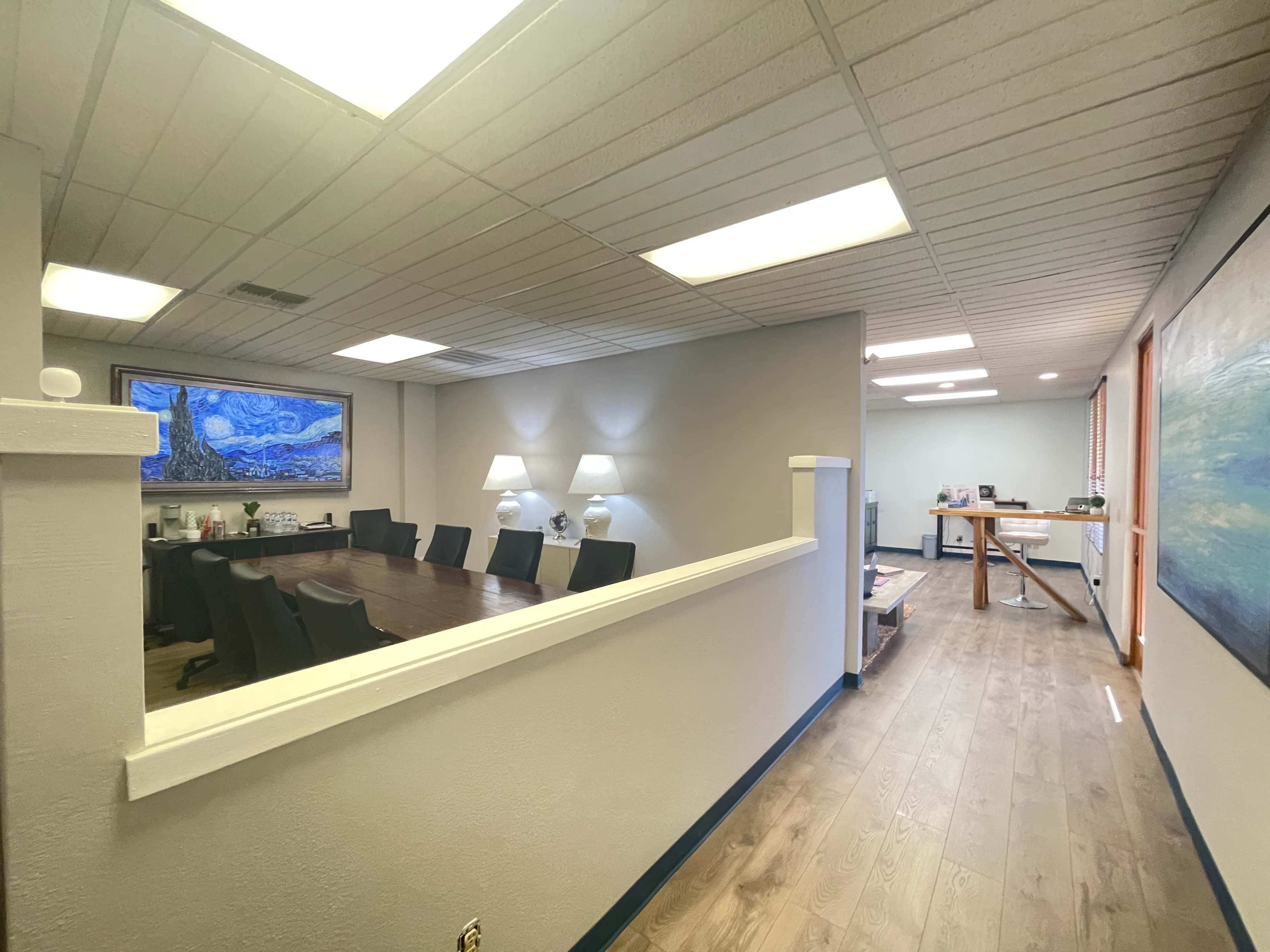 A well-lit office space with a conference room on the left and an open area leading to additional workspaces on the right.