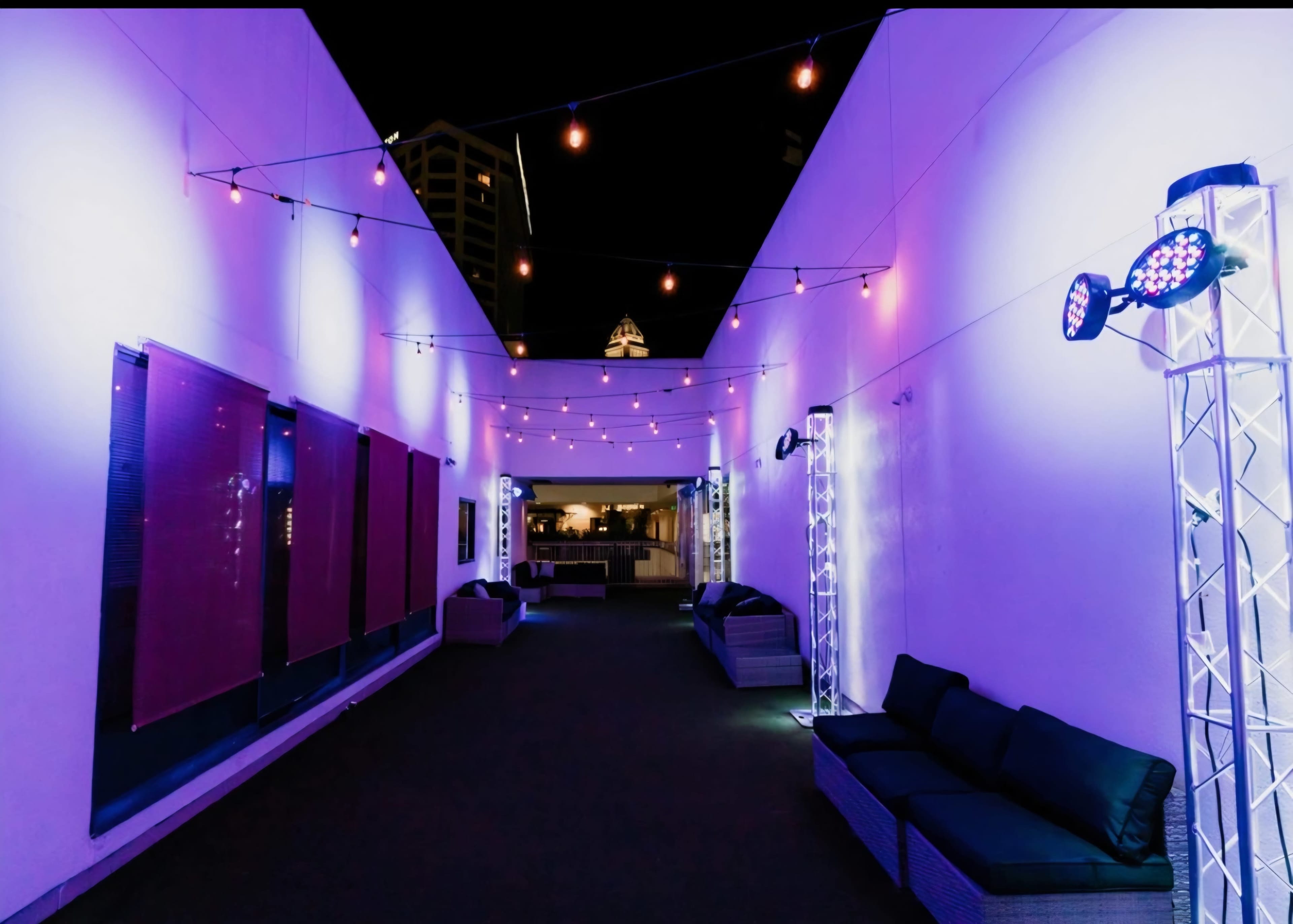 The image shows a lighted outdoor corridor with seating on both sides, illuminated by purple and white lights.