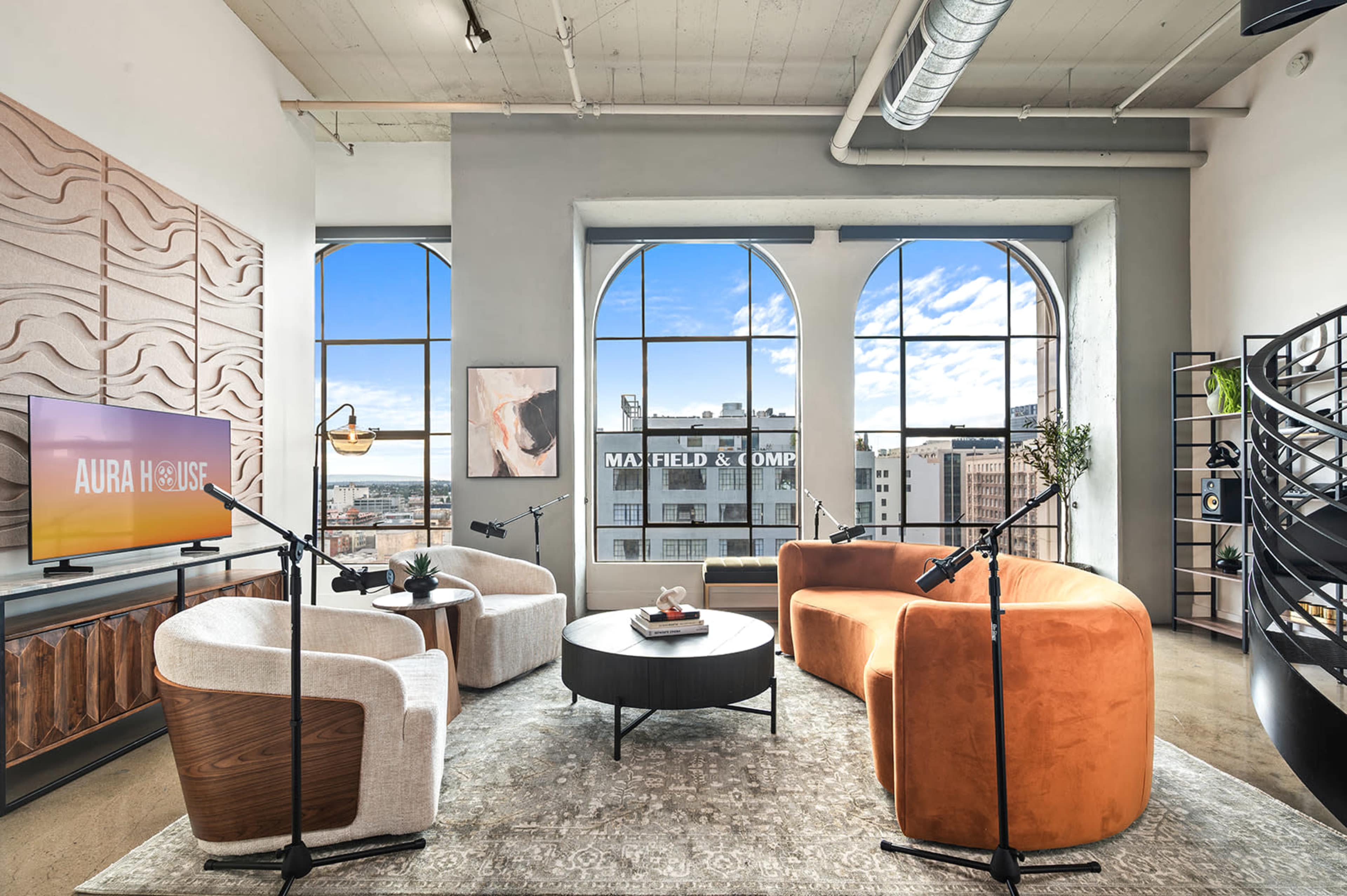The image showcases a modern living room with large arched windows, stylish furniture including circular chairs and a coffee table, and decorative elements such as a television and a spiral staircase.