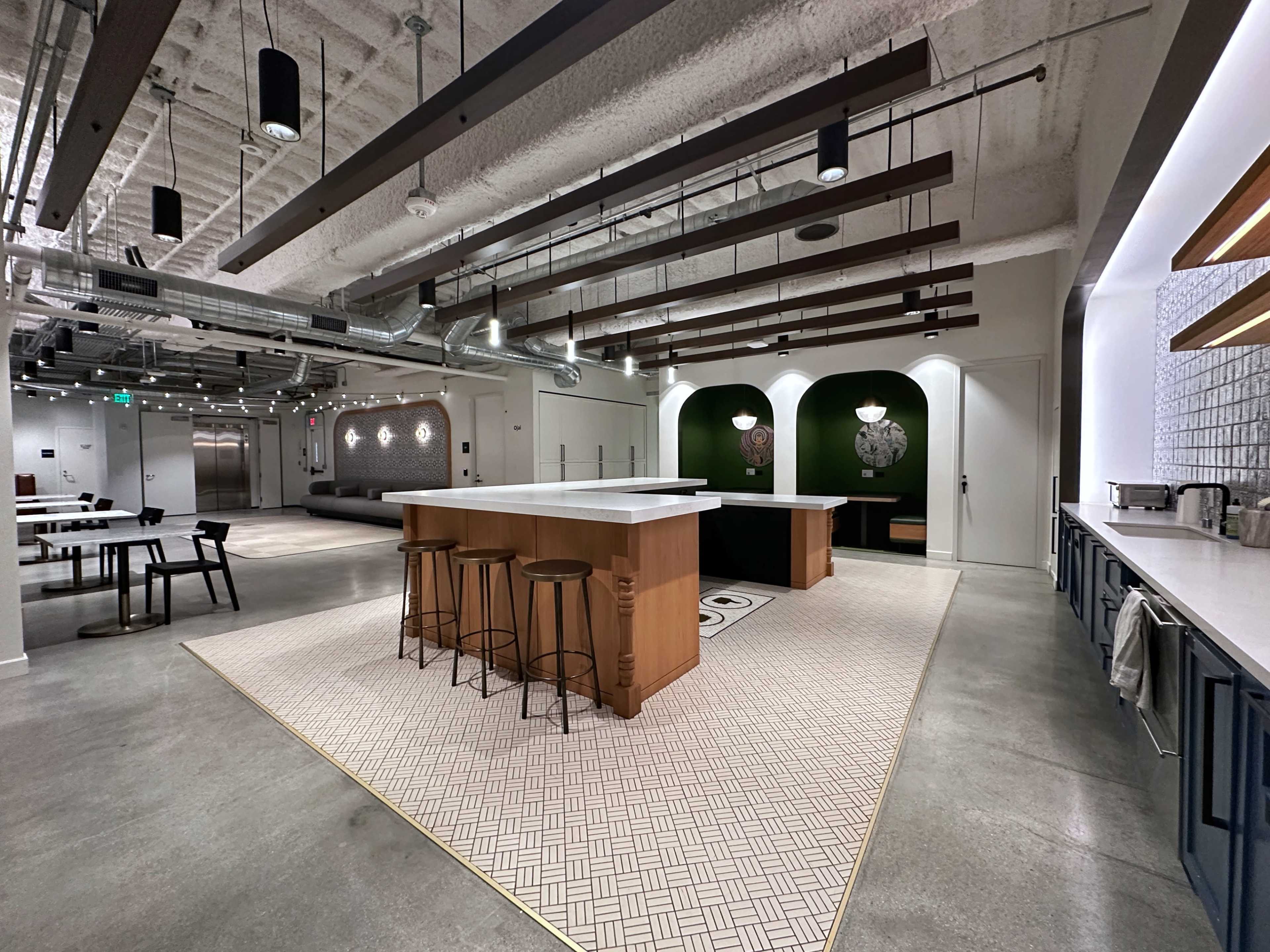 A modern kitchen area with a large central island, bar stools, and a clean, minimalist design featuring geometric patterns on the floor.