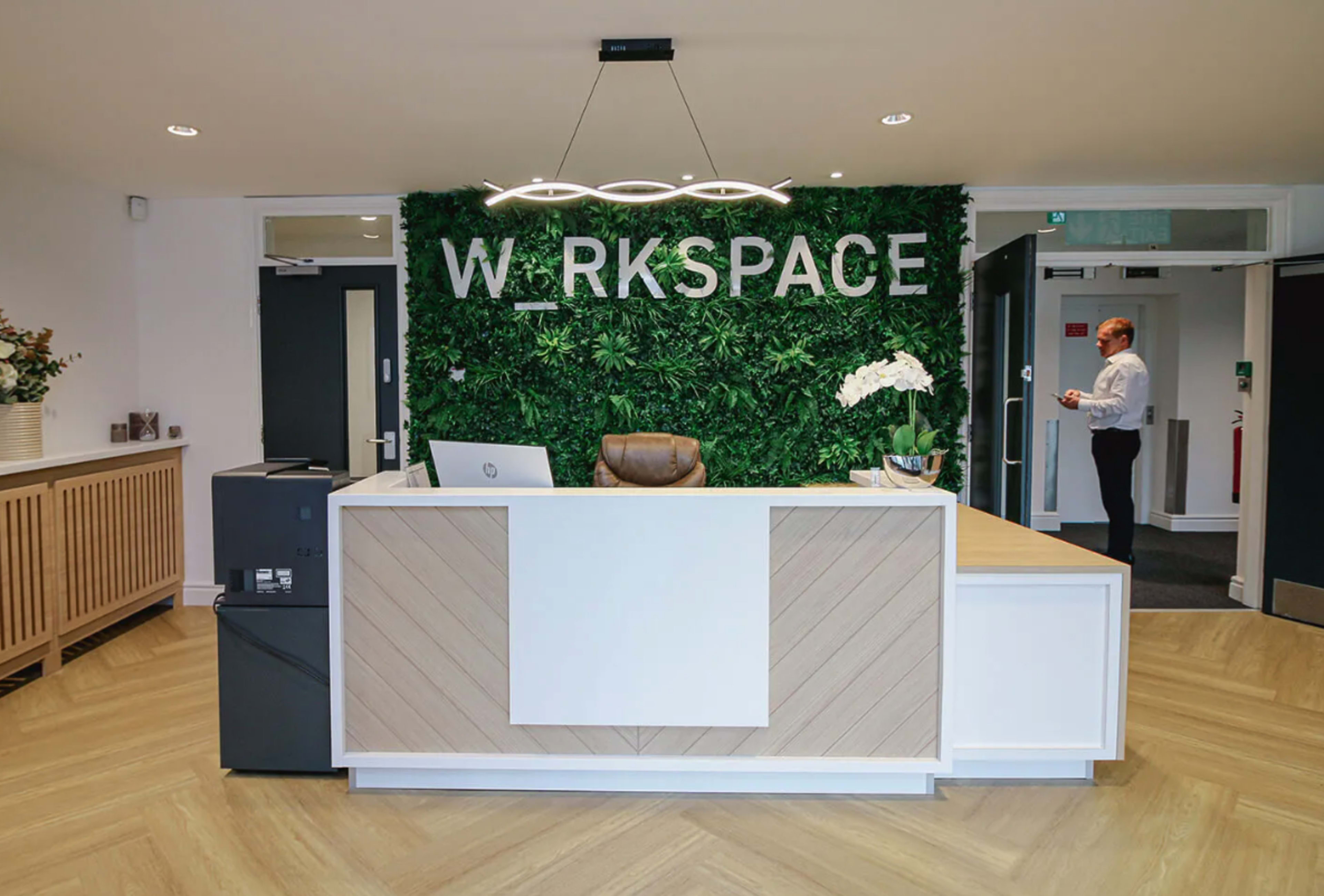 The image shows a modern reception area with a greenery wall and the word "WORKSPACE" prominently displayed above the front desk.