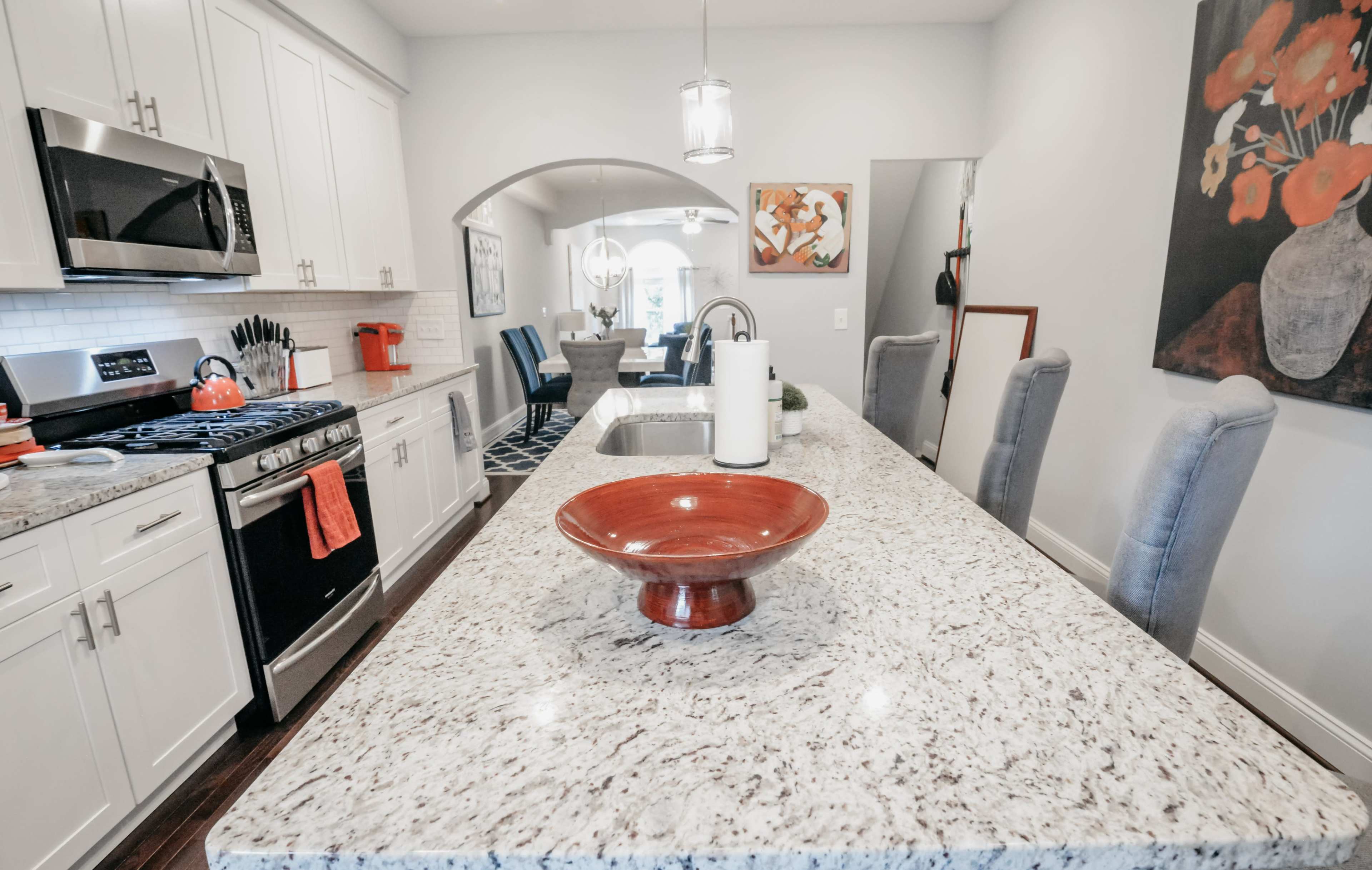 A modern kitchen features white cabinetry, stainless steel appliances, and a speckled granite island with a central red bowl.