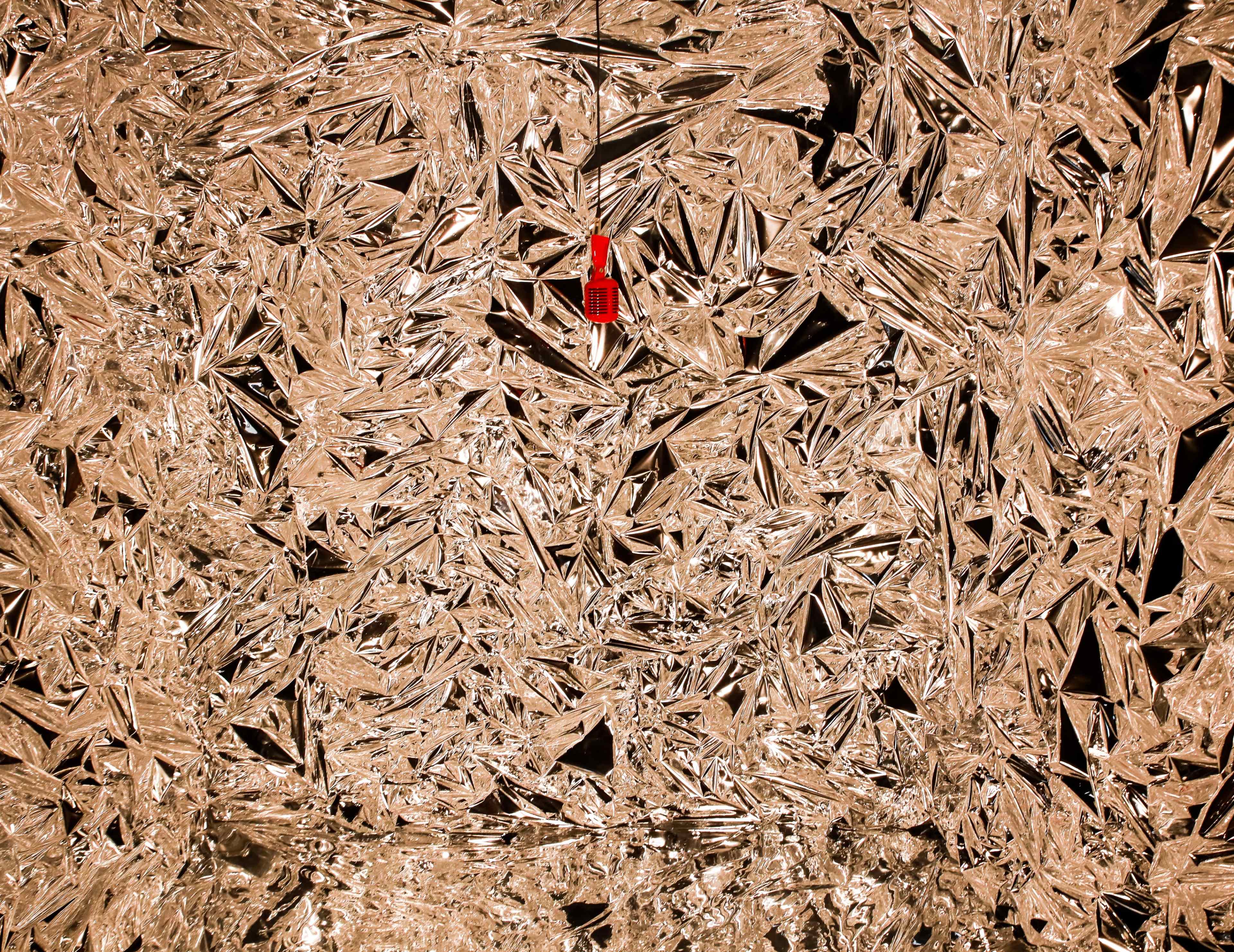 A small red object hangs against a background of crumpled, reflective foil resembling jagged ice.
