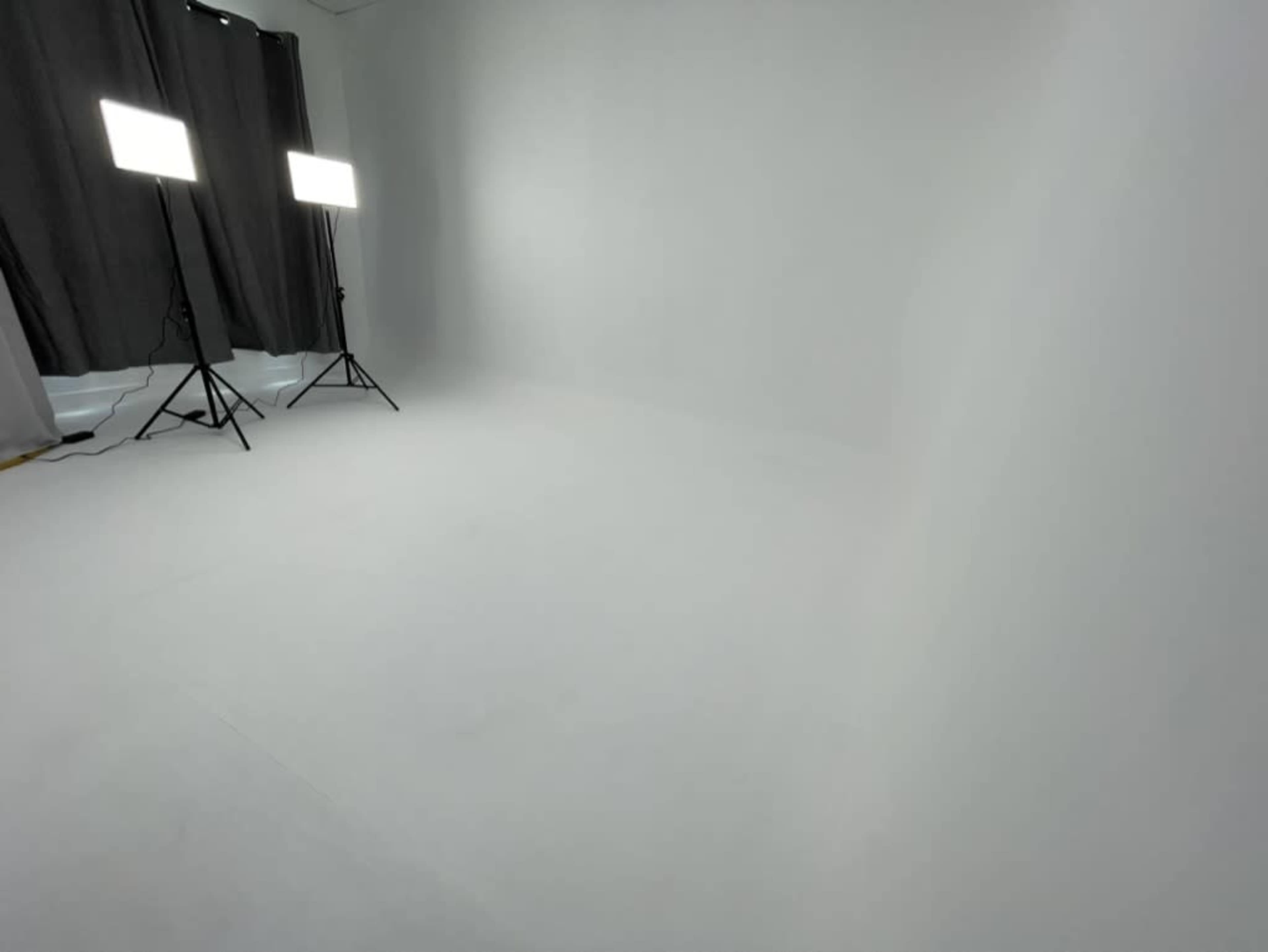 The image shows a spacious room with a white floor and white walls, illuminated by two softbox lights on tripods.
