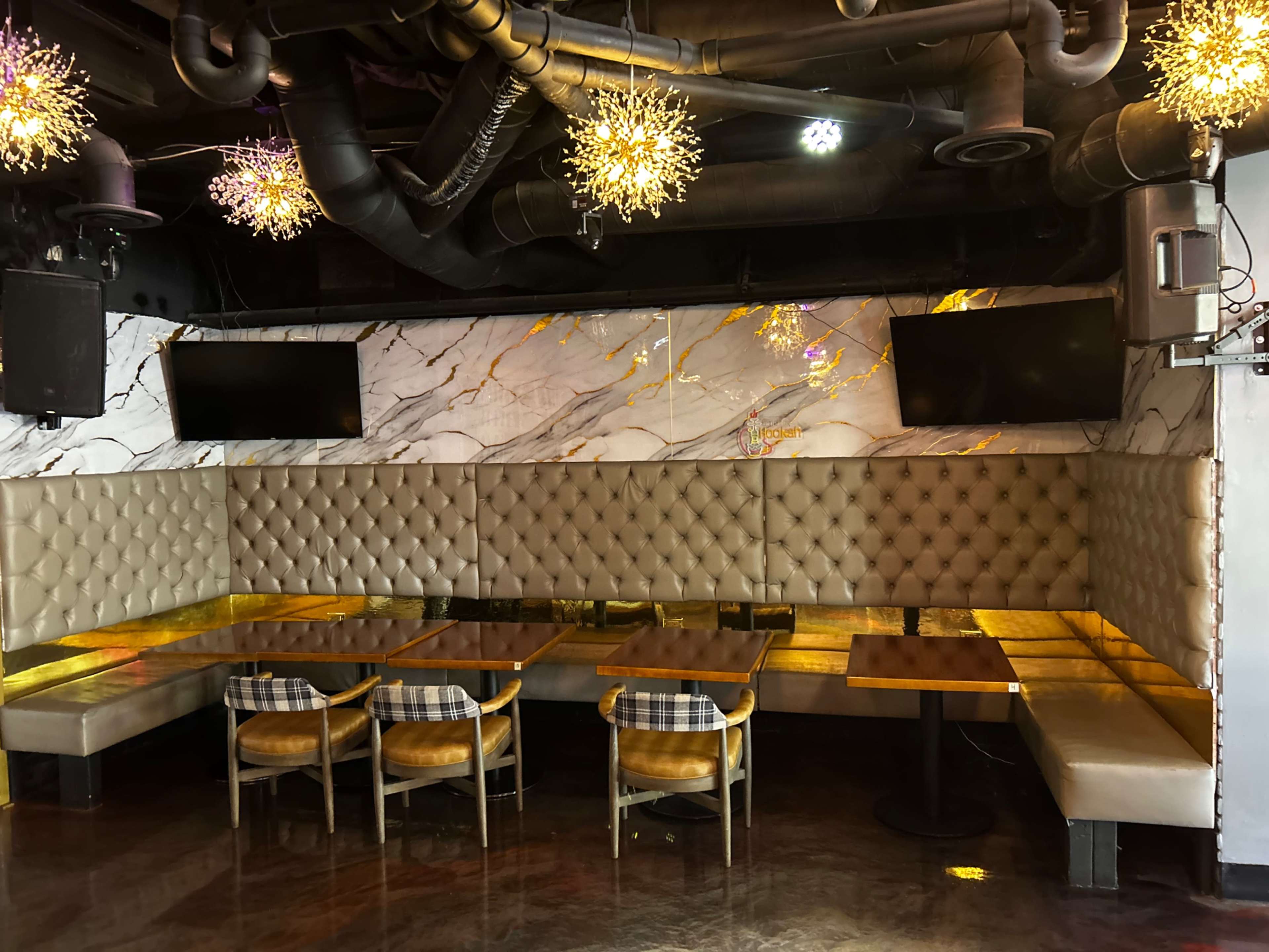 The image shows an empty restaurant booth area with marble-patterned walls, golden accents, and two television screens mounted on the wall.