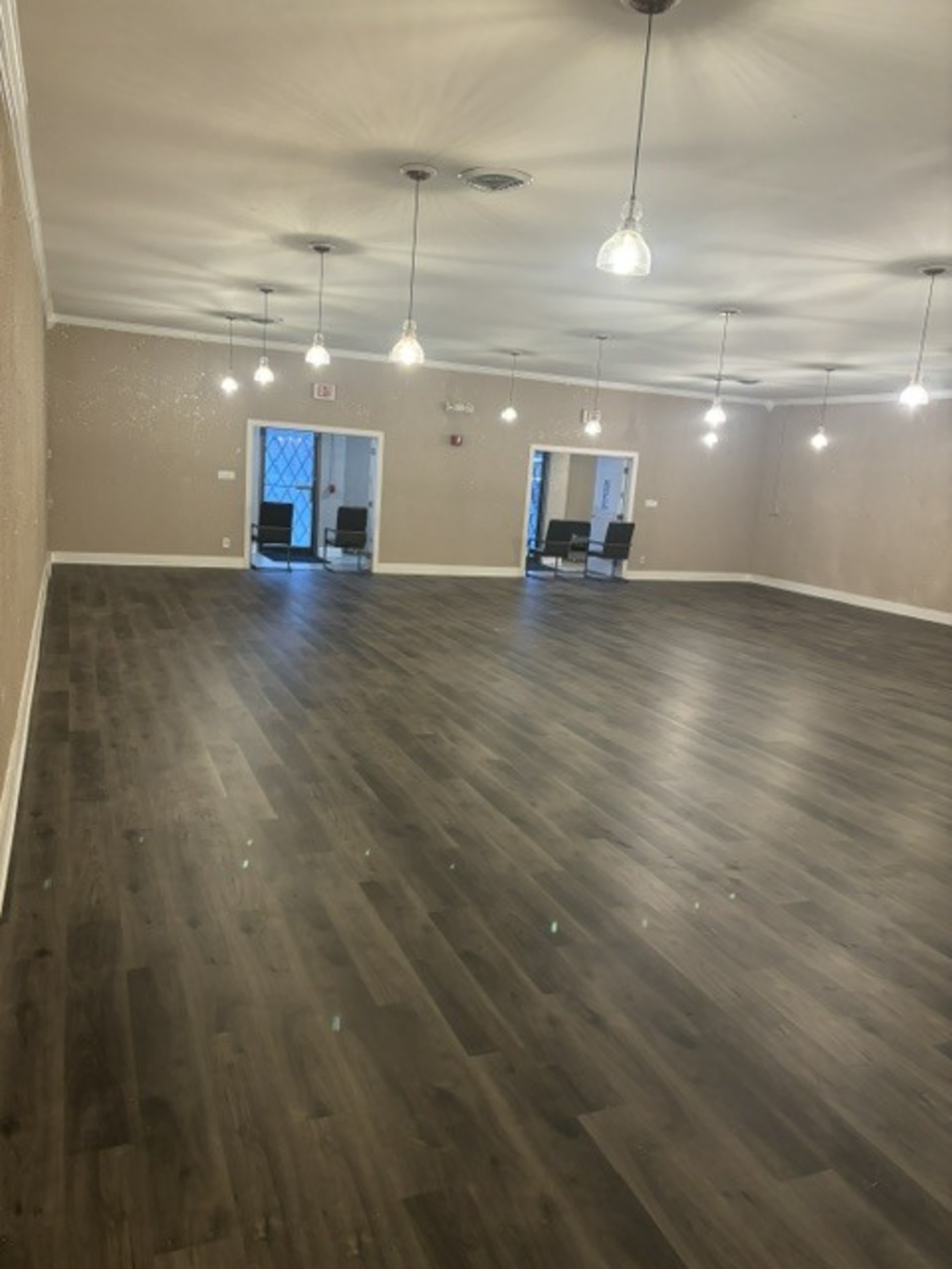 The image shows a spacious room with wooden flooring, walls painted in a light color, and several pendant lights hanging from the ceiling.