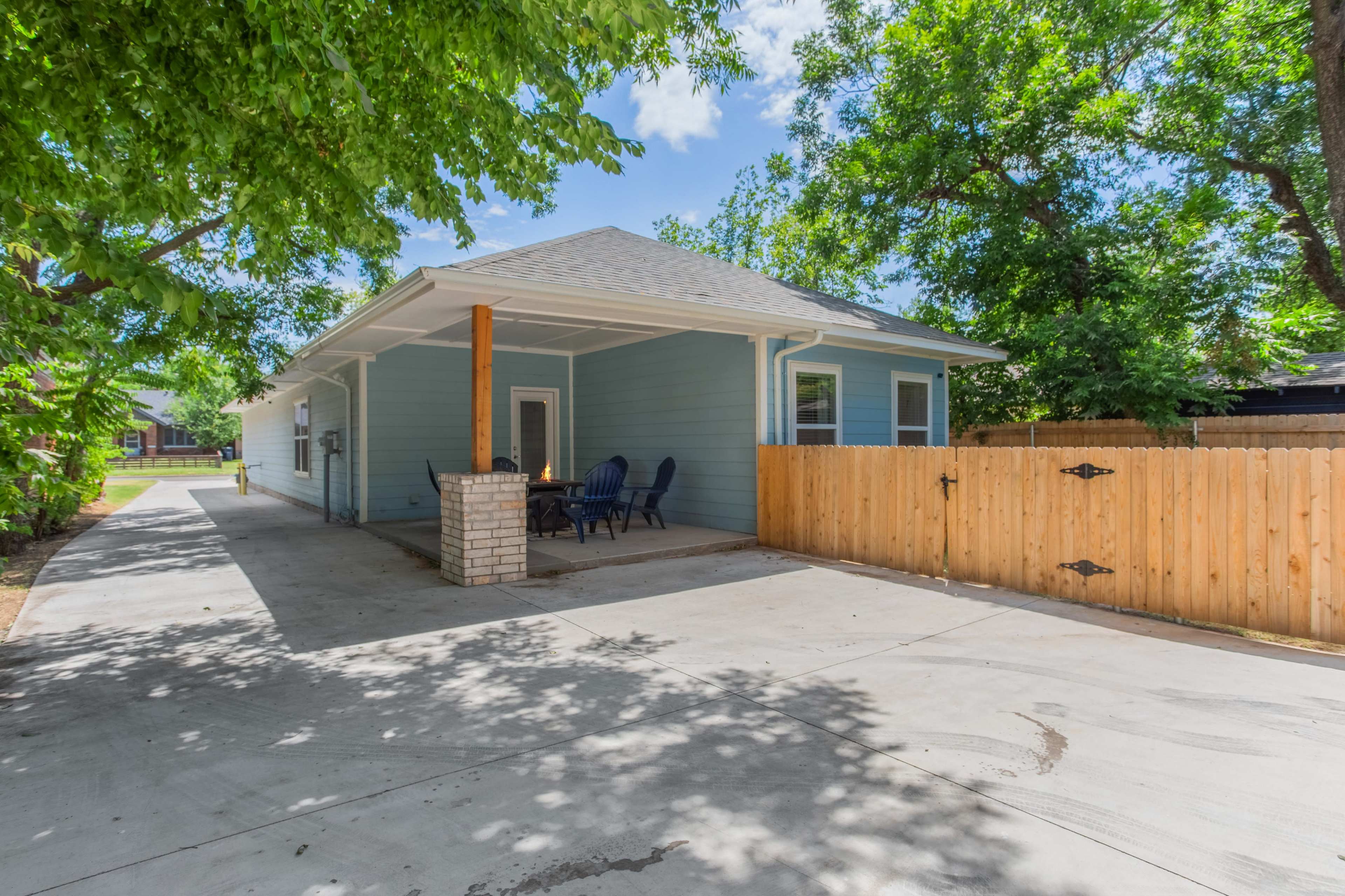 A light blue house with a porch and a fenced yard sits under green trees.