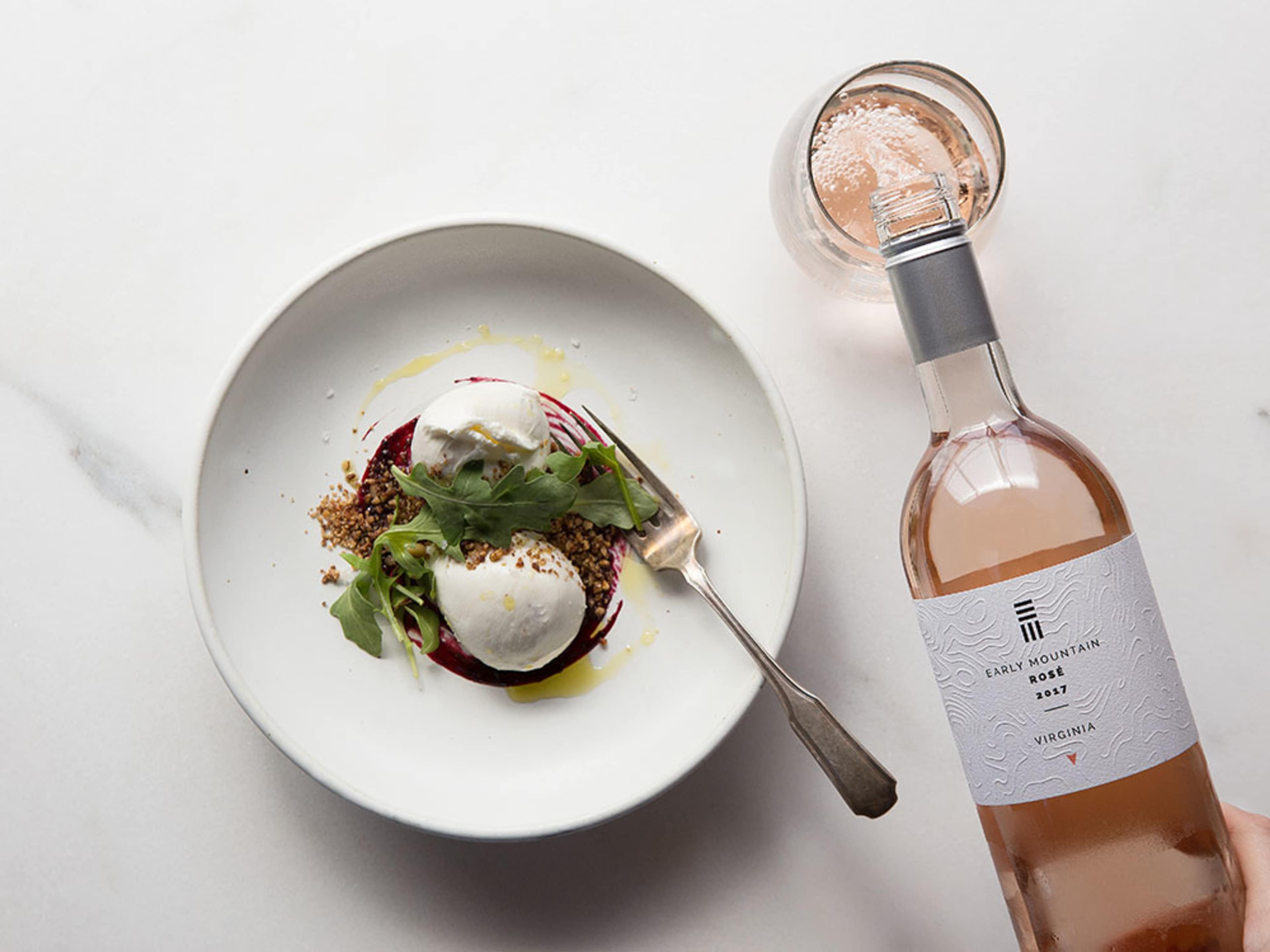 A plate of salad with beets, goat cheese, and arugula is accompanied by a bottle of Early Mountain rosé wine and a glass of the same.