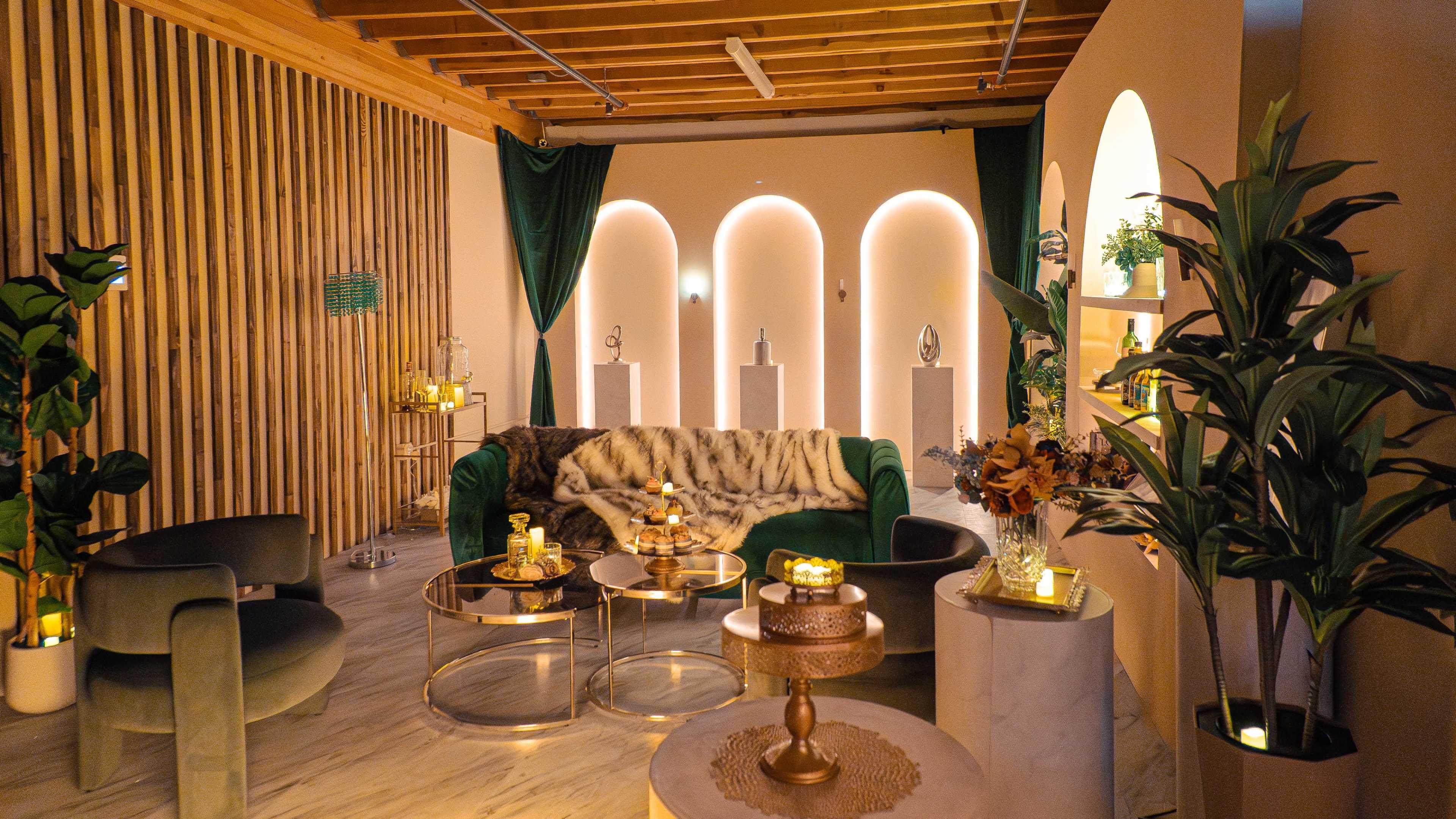 The image shows a modern lounge area featuring a green velvet sofa, elegant decor, and ambient lighting elements.