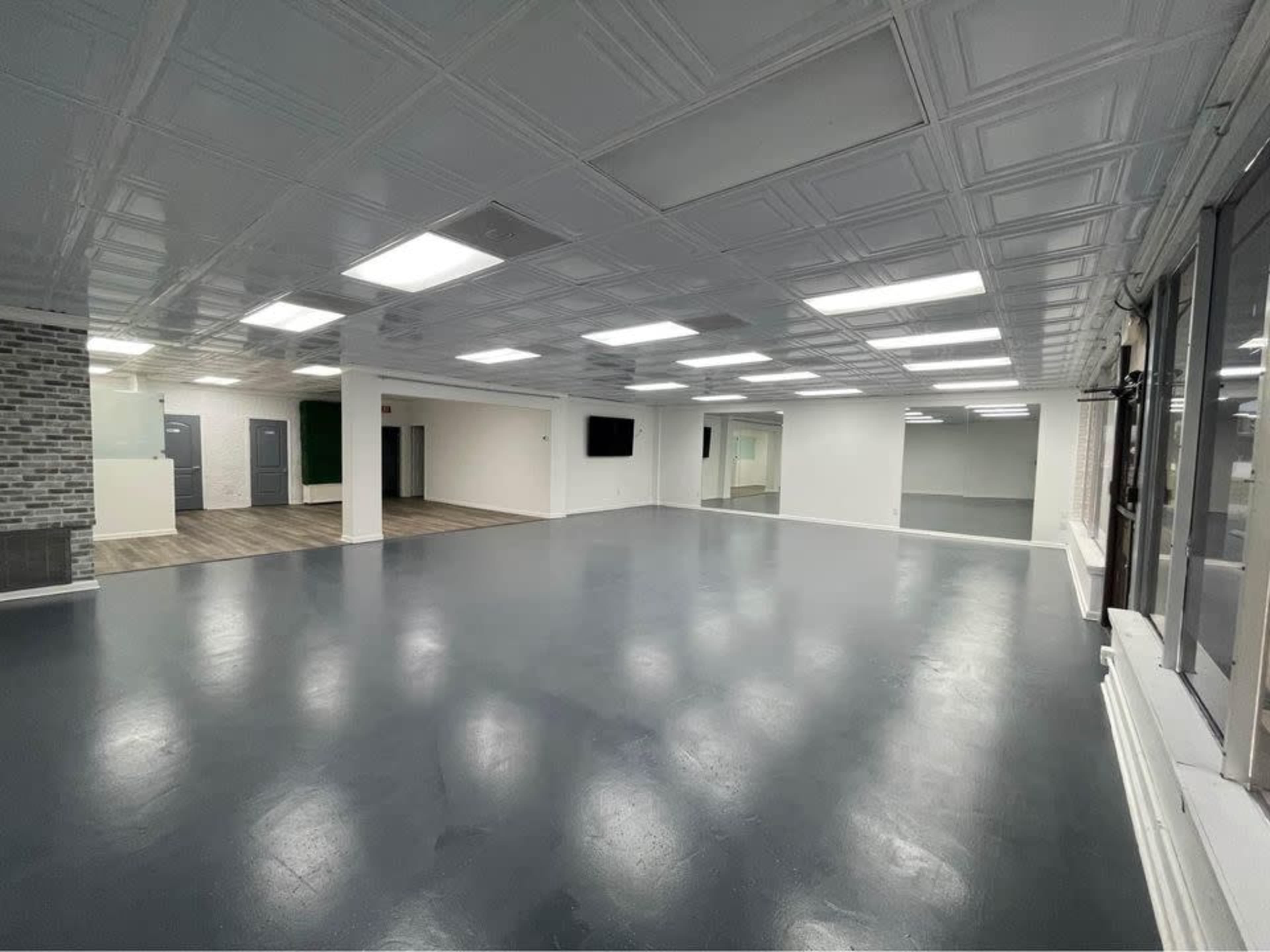 The image showcases a spacious, empty room with a polished floor, bright ceiling lights, and large windows.