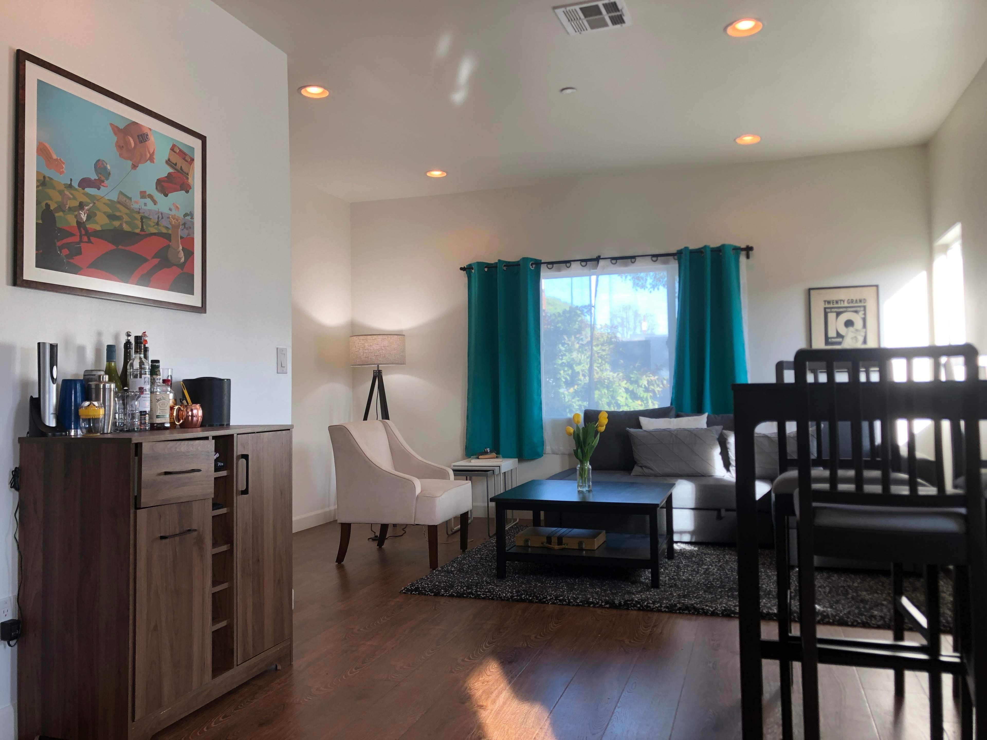 The image shows a modern living room with a light-colored sofa, a coffee table, and decorative elements, including a lamp and a bar cabinet.
