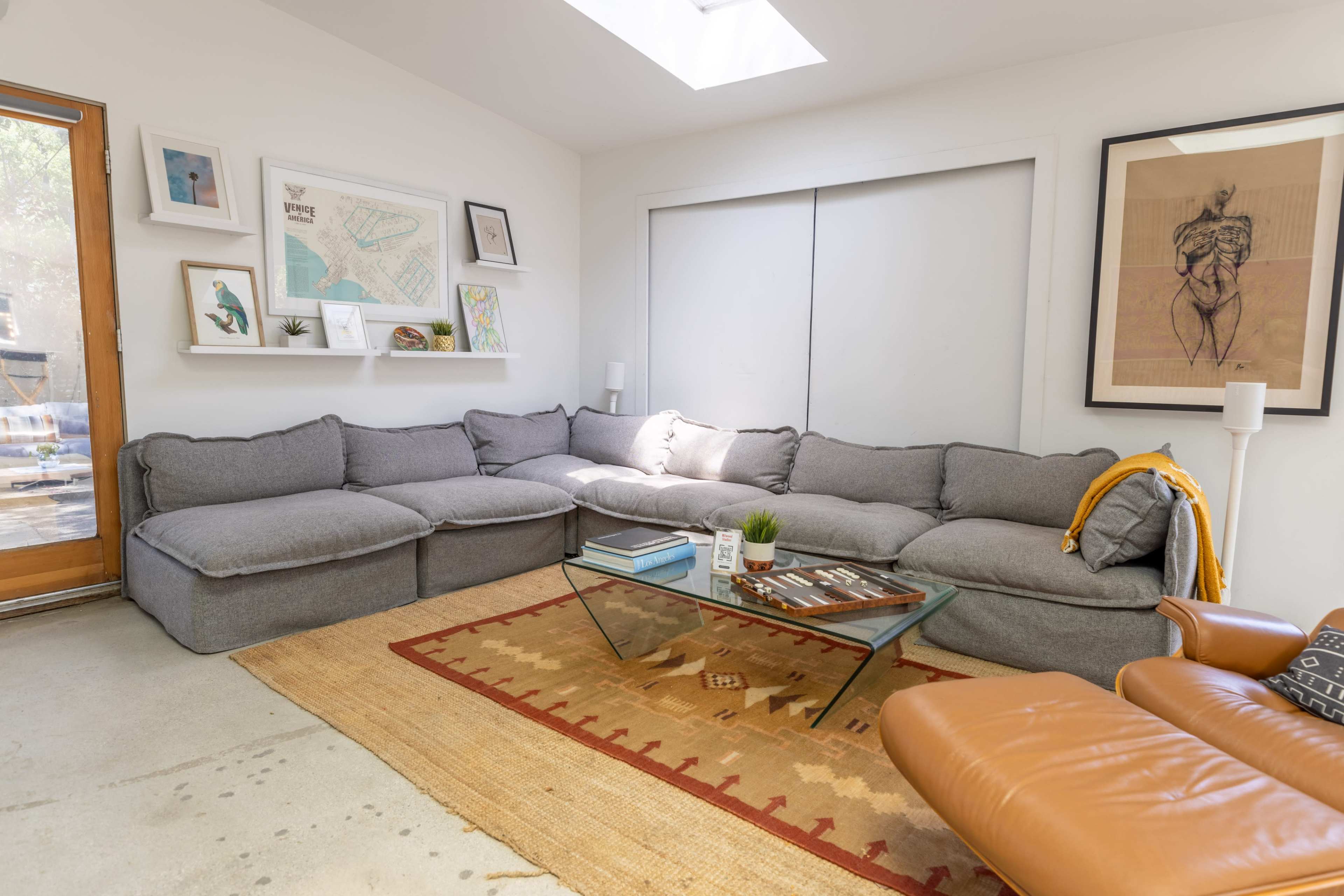 A modern living room with a gray sectional sofa, a glass coffee table on a patterned rug, and a wooden door leading outside.