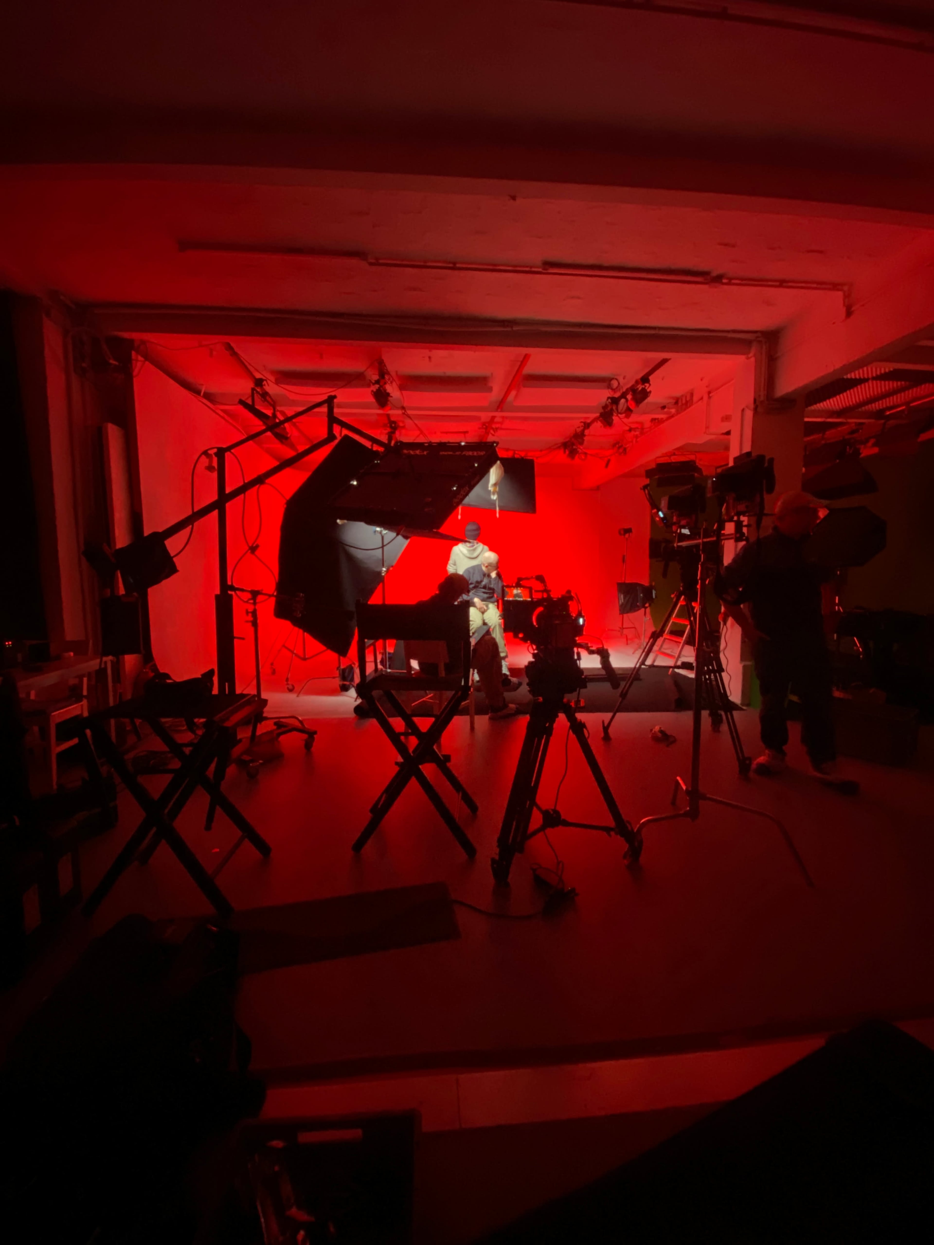 A photography studio is illuminated with red lighting, featuring multiple cameras and equipment set up for a shoot.