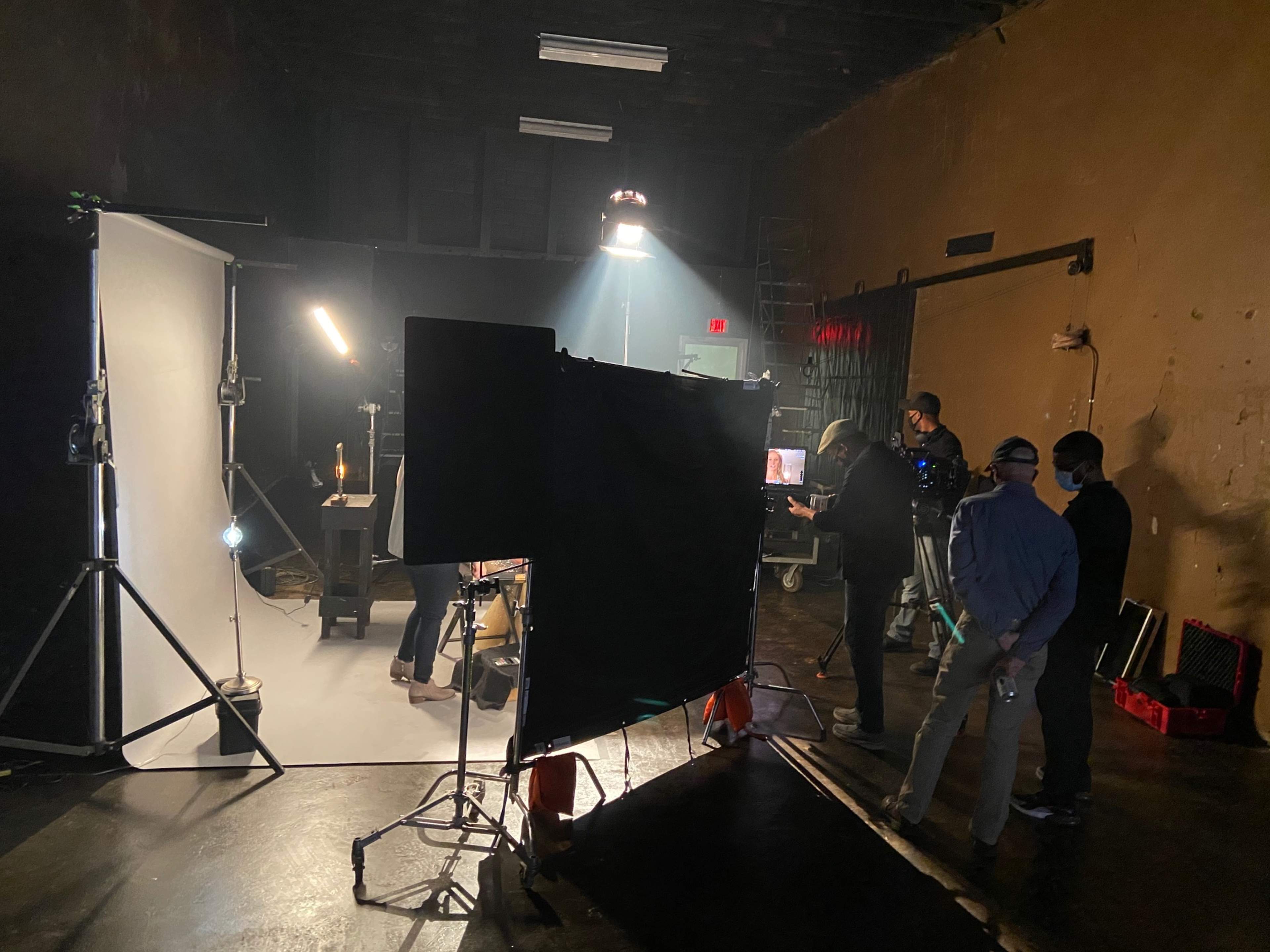A group of people set up equipment in a studio for a photoshoot, with a backdrop and lighting rig in place.