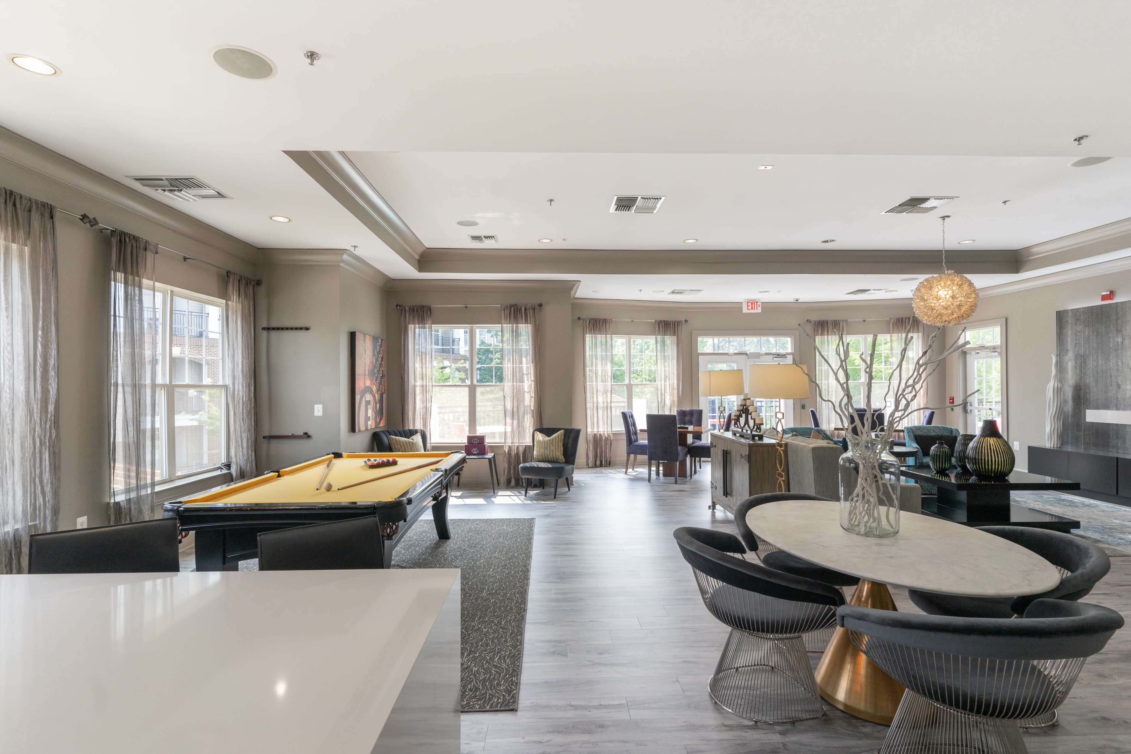 The image features a modern interior space that includes a pool table, dining area, and seating arrangement, illuminated by natural light from large windows.