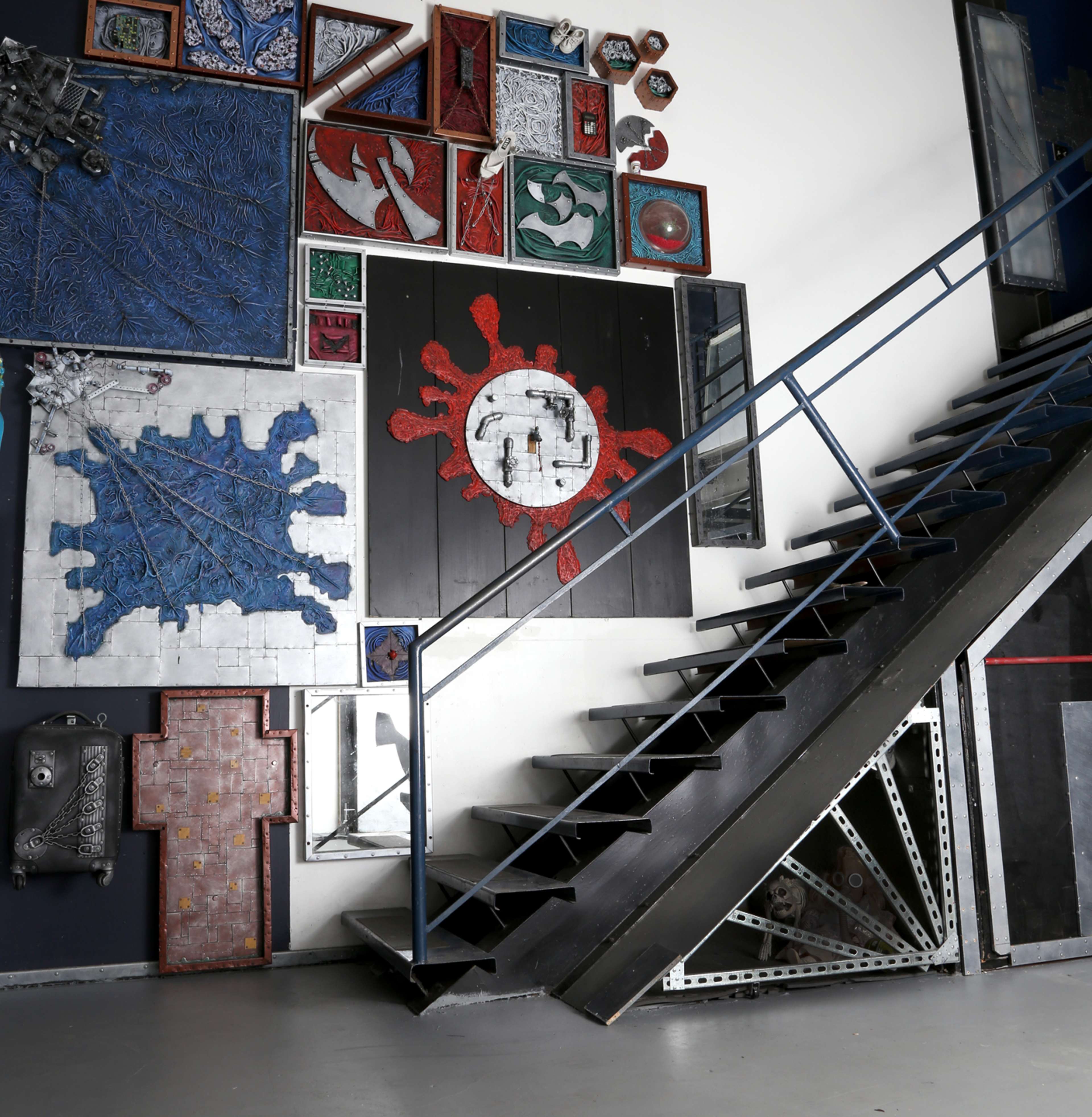 A metal staircase leads to an upper level beside a wall adorned with various colorful artworks and frames.