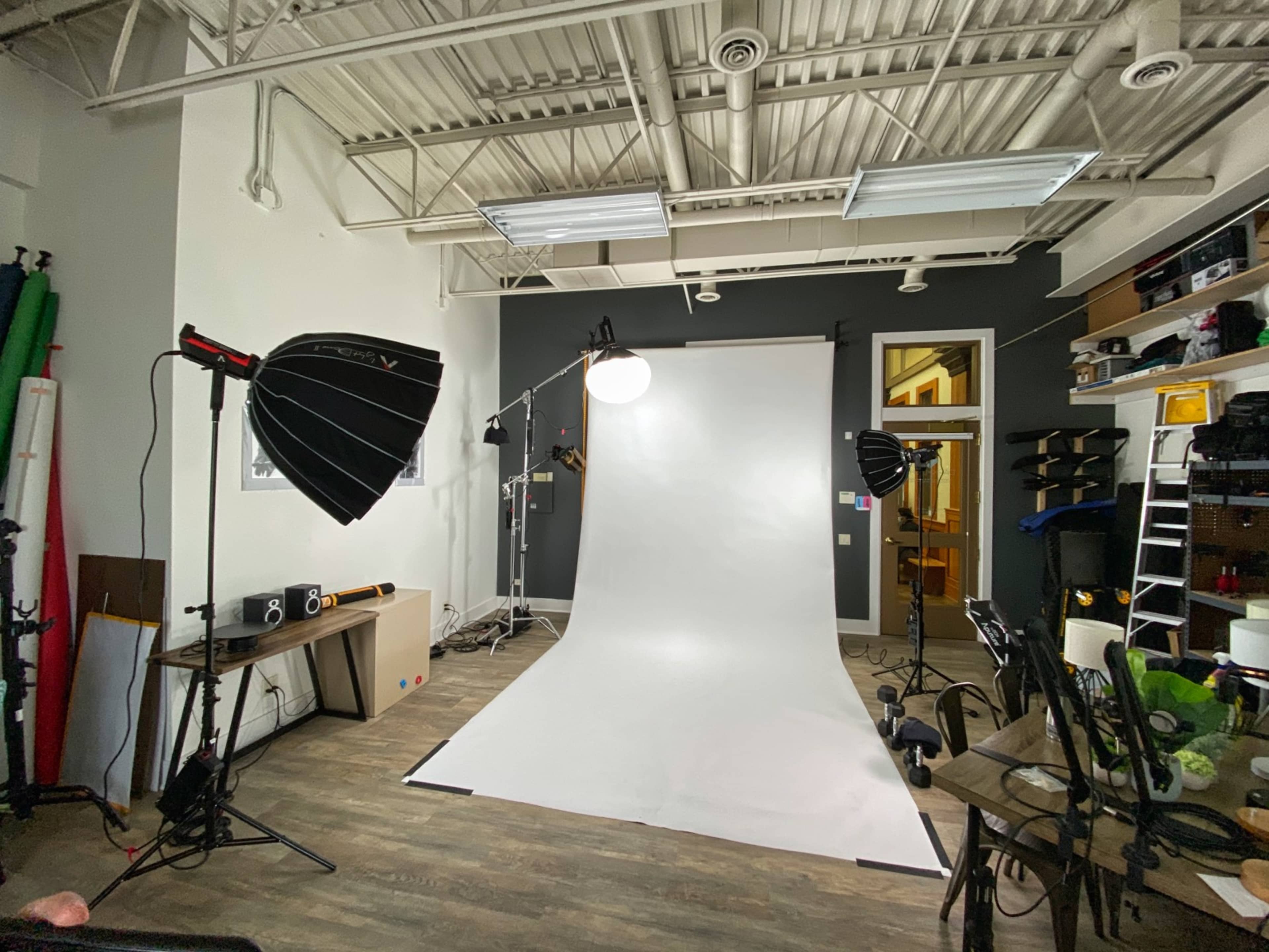 A photography studio is equipped with a white backdrop, lighting equipment, and various props arranged around the space.