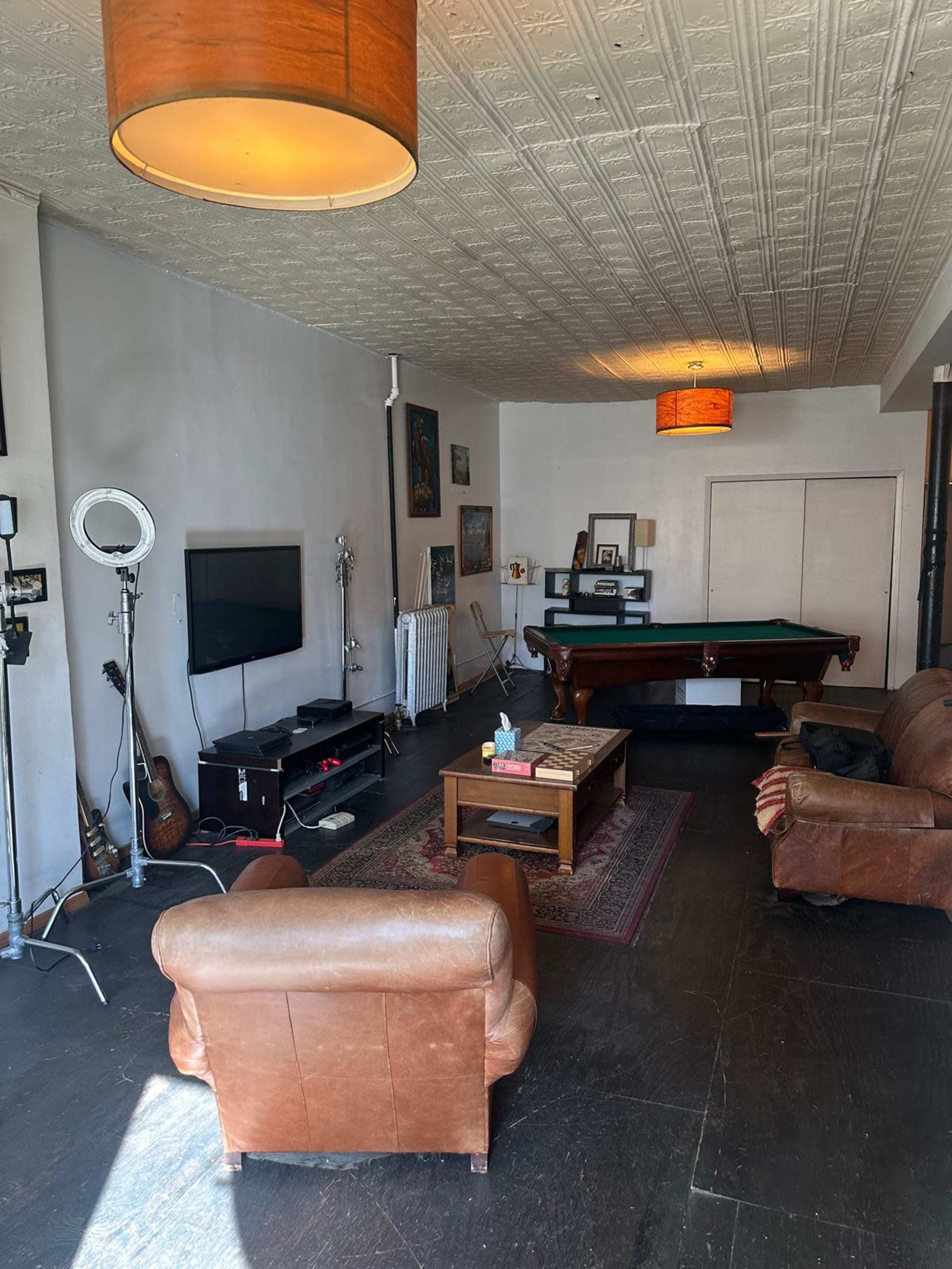 The image shows a living room with a pool table, two leather armchairs, a coffee table, and a television against one wall.