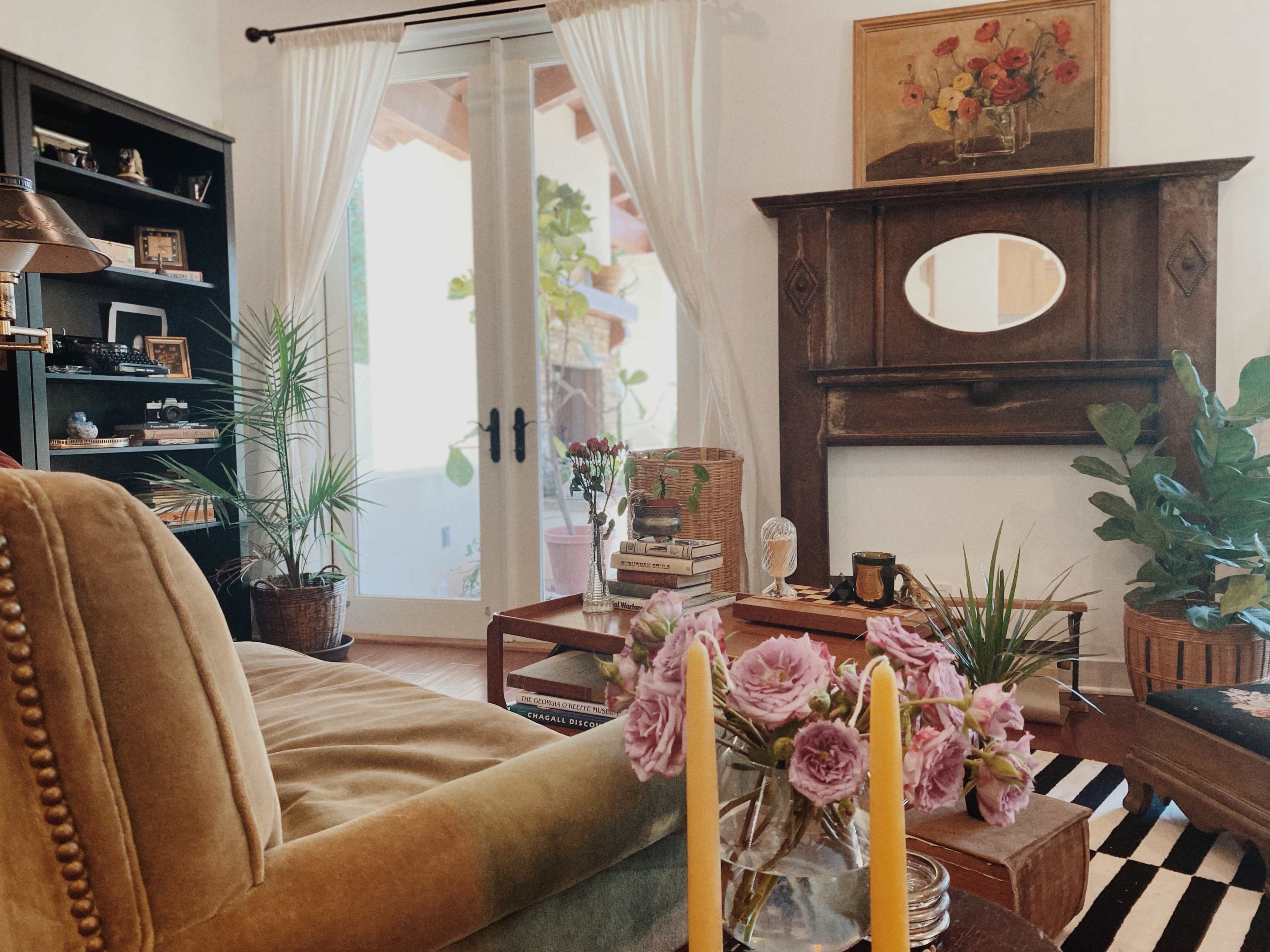 A cozy living room featuring a green sofa, a wooden coffee table, and a decorative fireplace with an oval mirror above it.