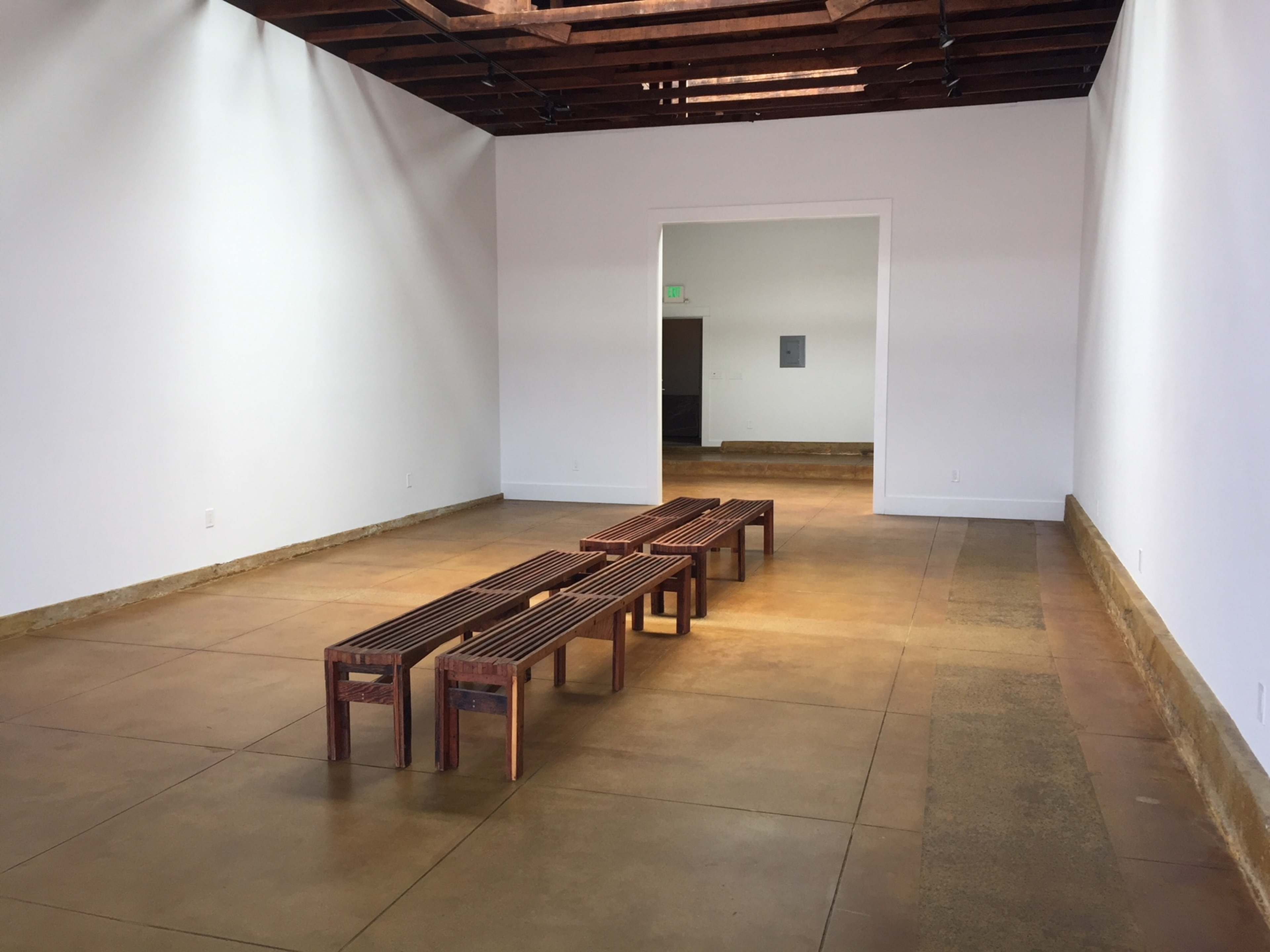 An empty art gallery features a wooden bench in the center and a doorway at the far end.