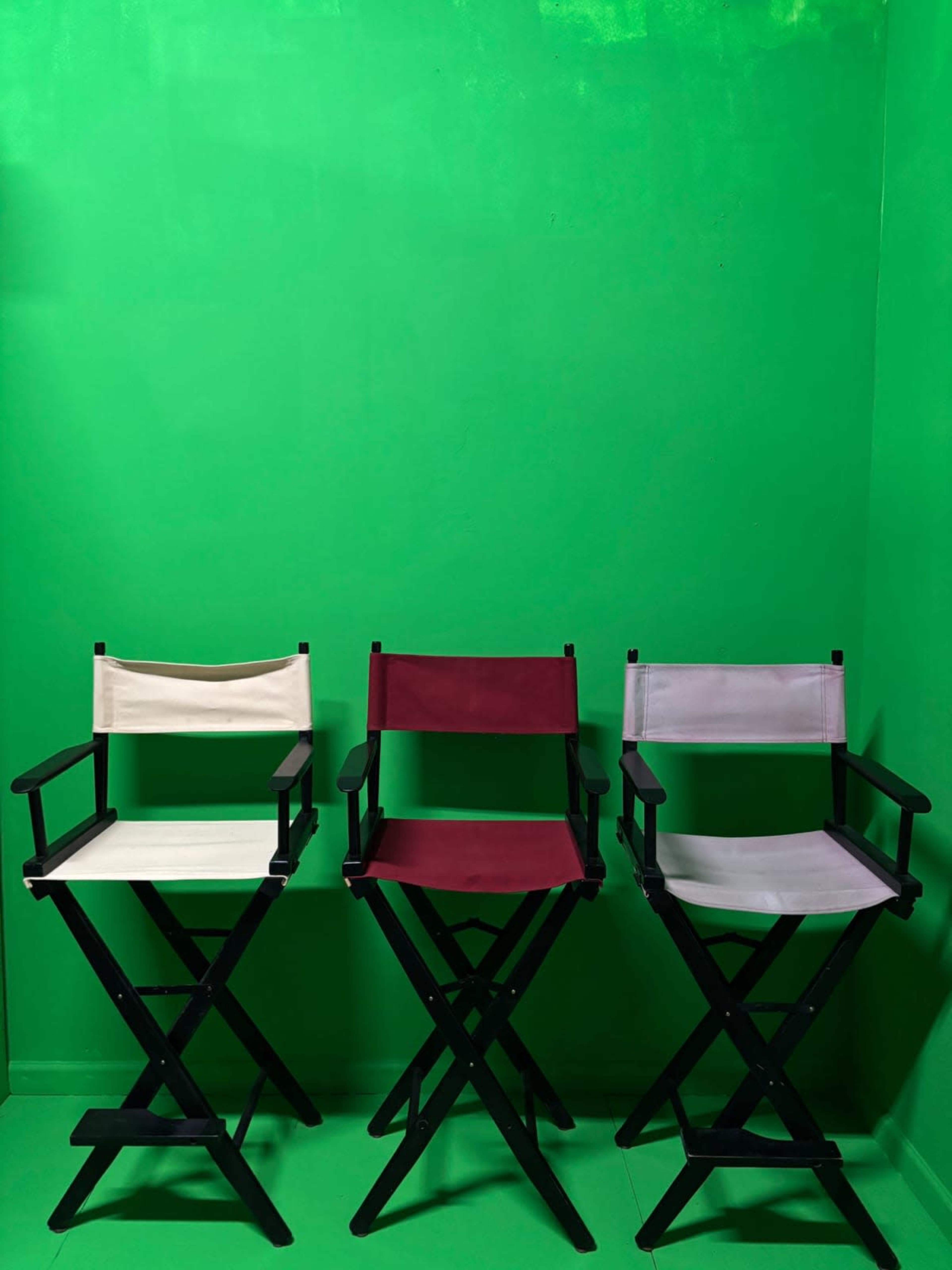 Three director's chairs in white, burgundy, and gray are set against a green backdrop.