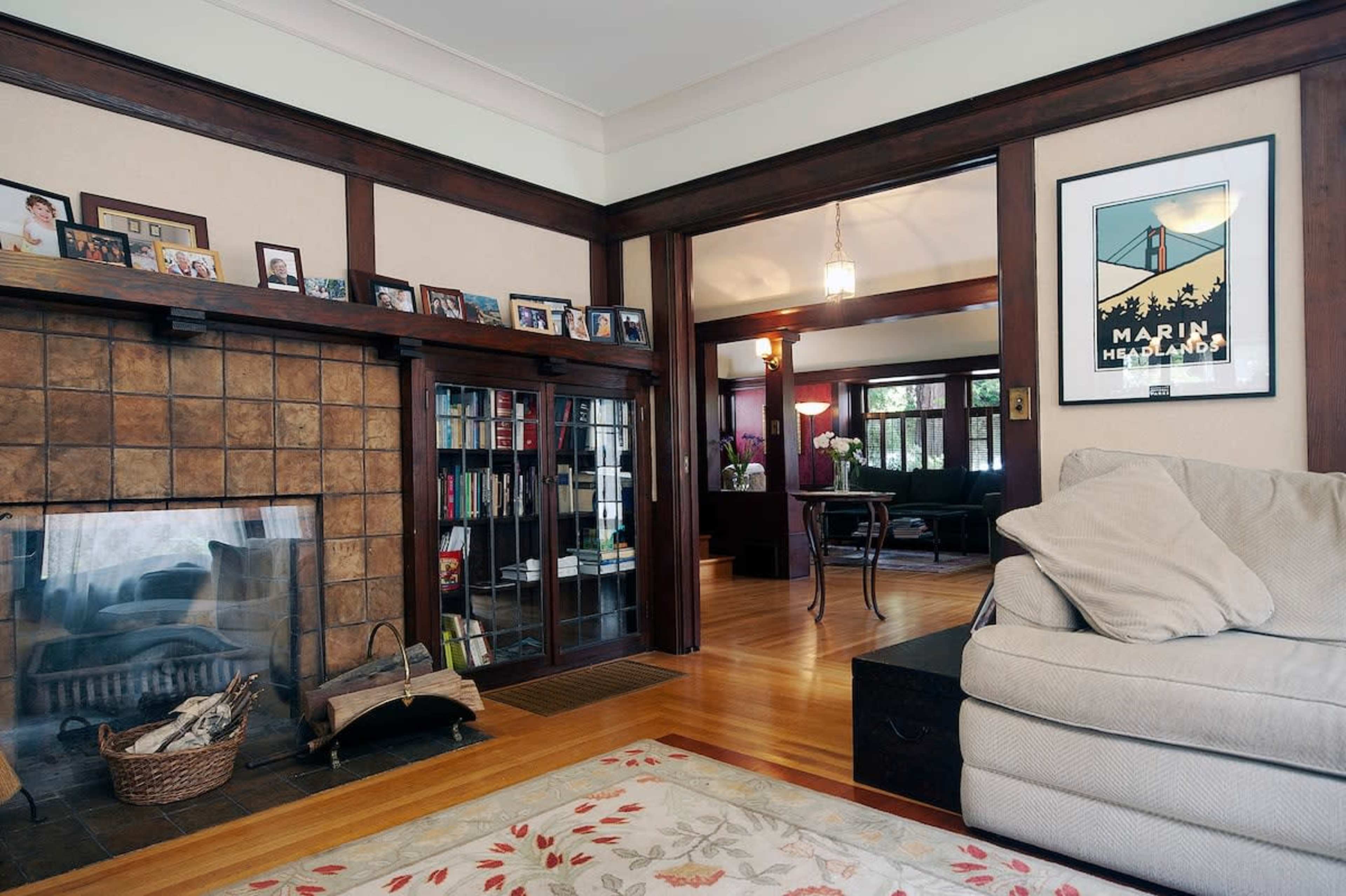 A cozy living room with a stone fireplace, bookshelves, and a large sofa, leading to another room in a home.