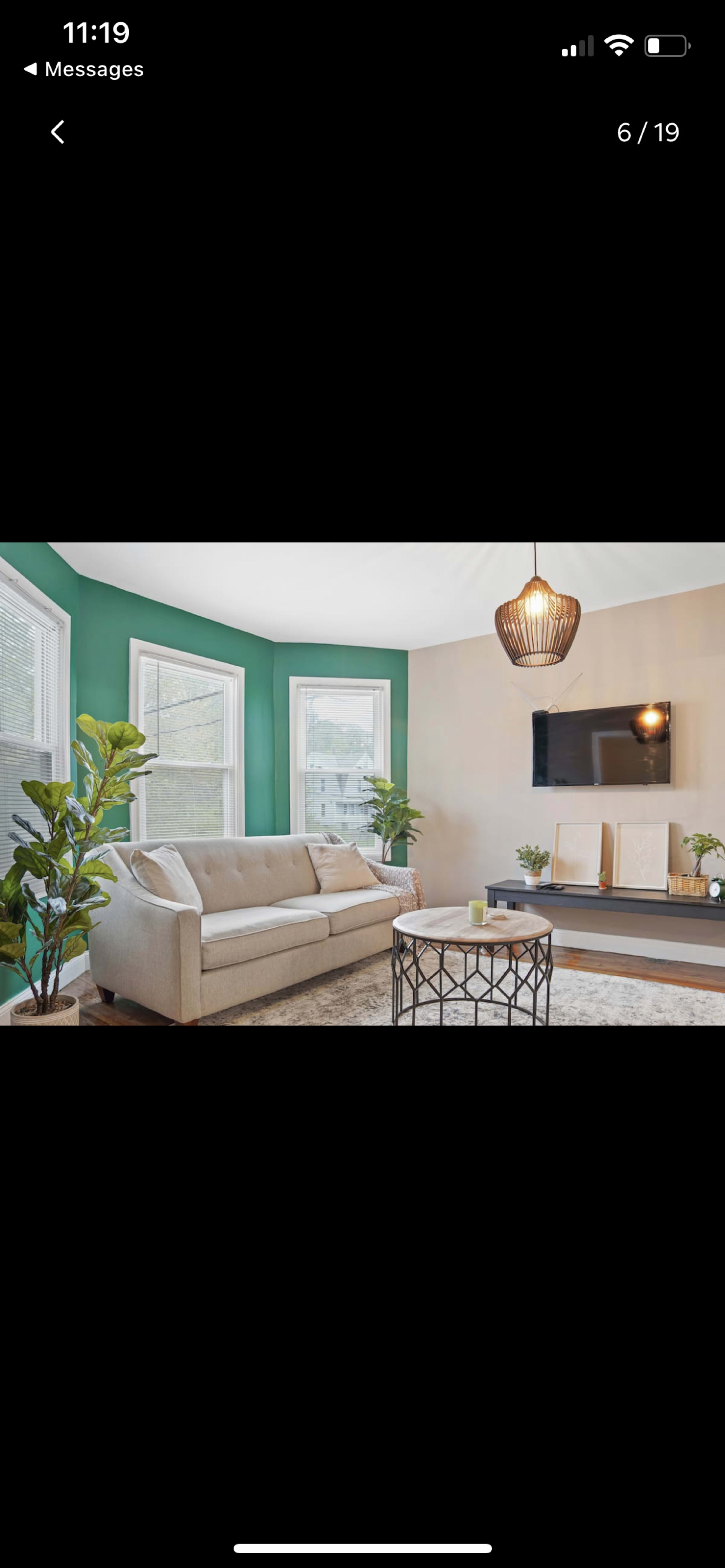 The image shows a modern living room with a light-colored sofa, a coffee table, plants, and a wall-mounted TV against a beige and green backdrop.