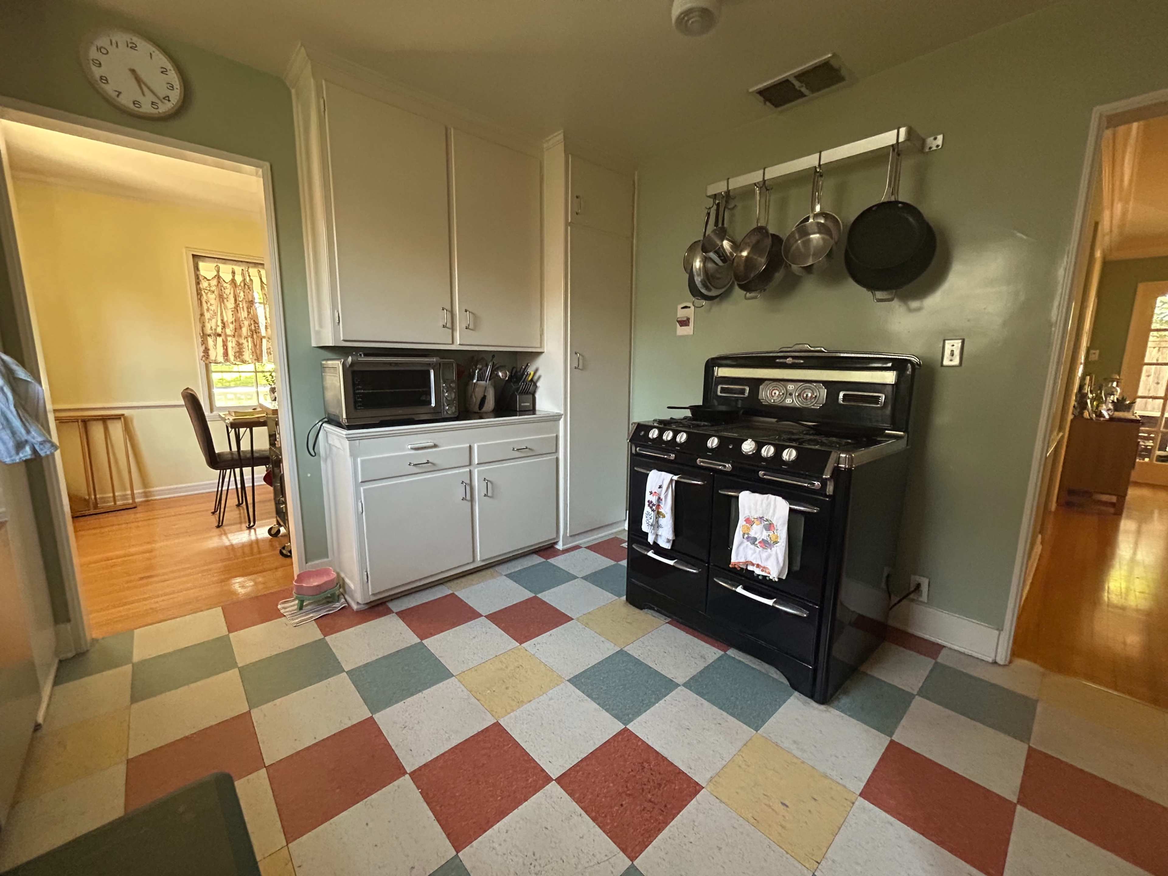 The image shows a retro-style kitchen with a black stove, checkered floor tiles in various pastel colors, and a microwave on the counter.