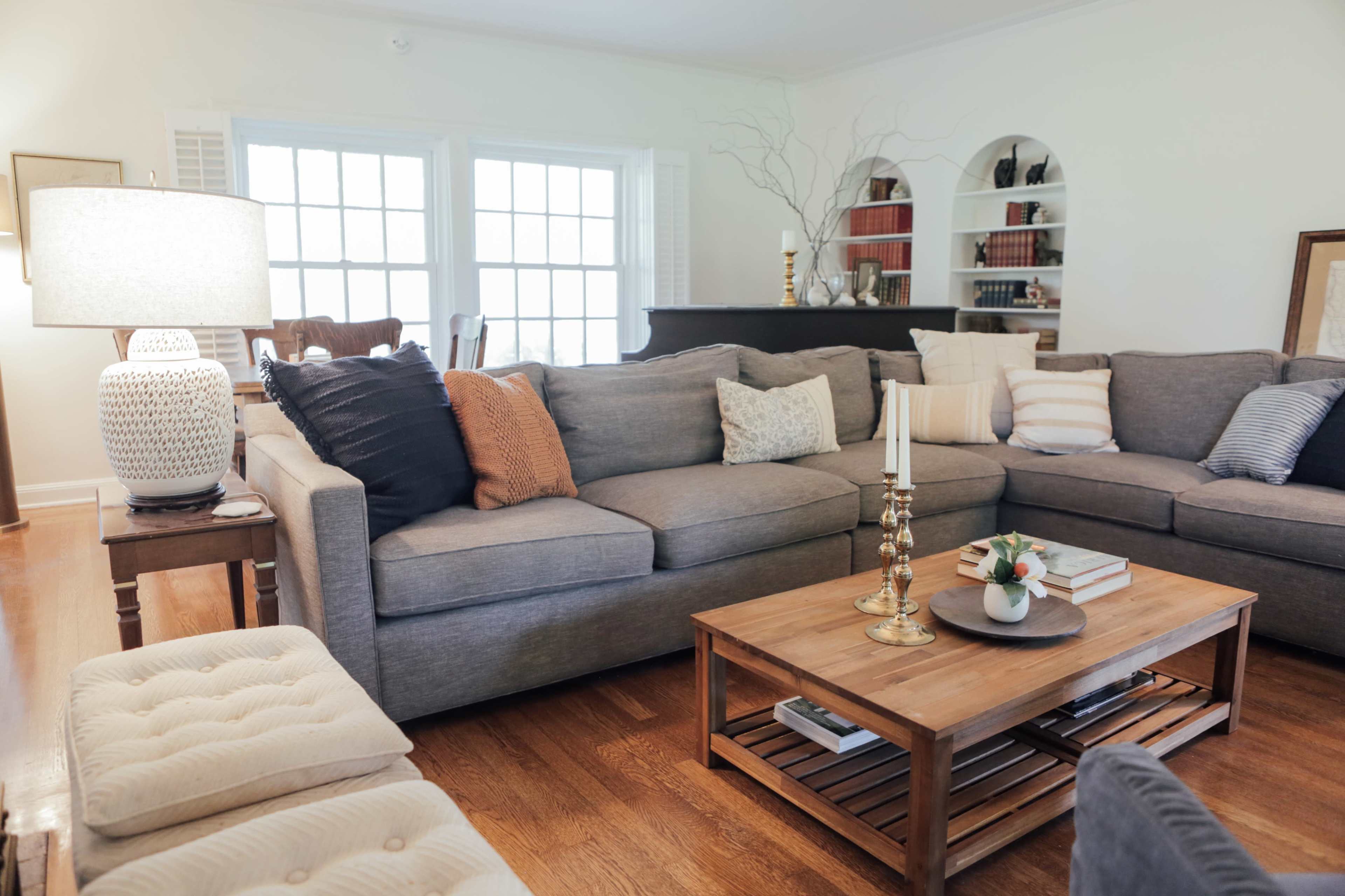 A spacious living room features a gray sectional sofa with various decorative pillows and a wooden coffee table at the center.