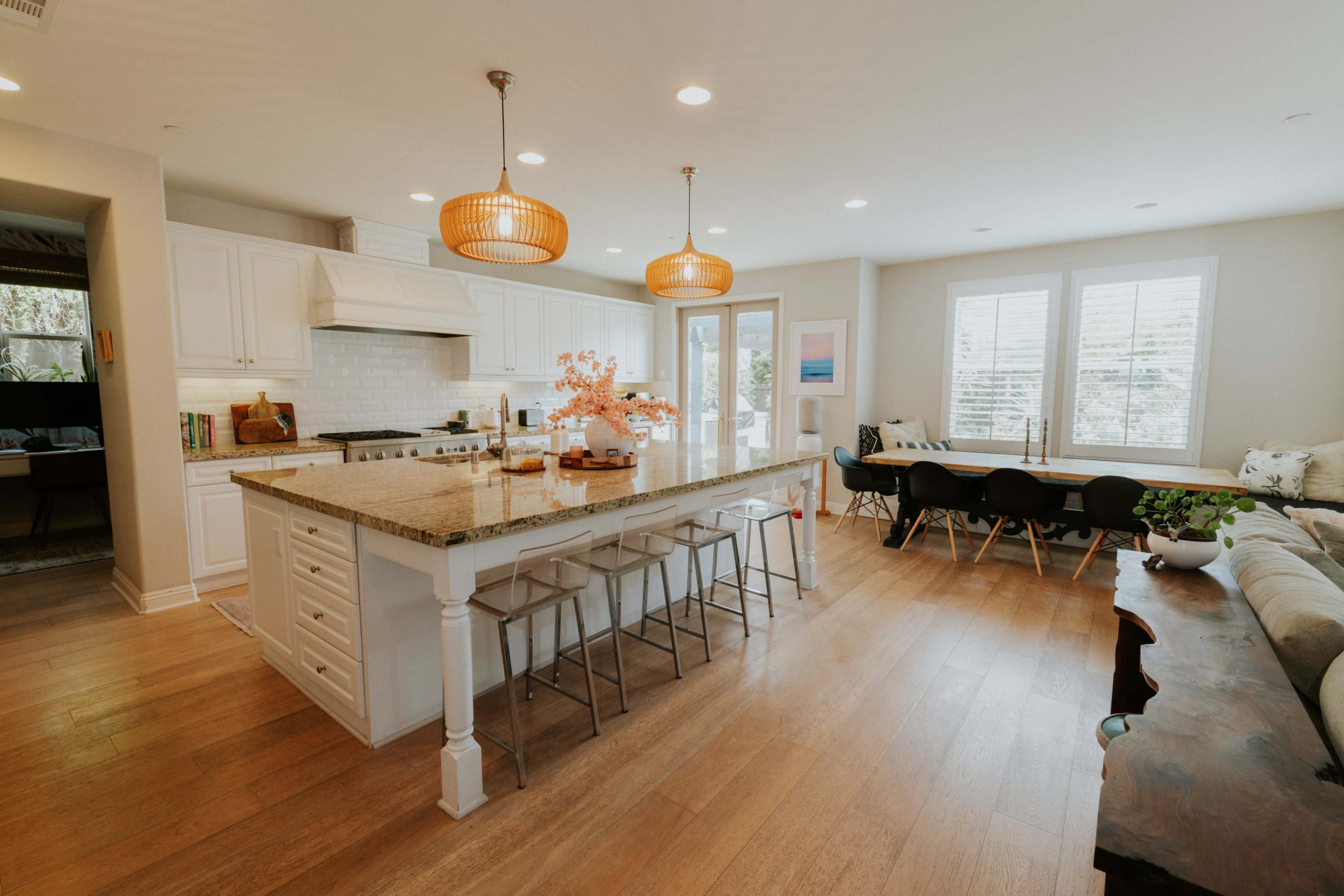 The image shows a modern kitchen and dining area featuring a large island with bar stools, white cabinetry, pendant lighting, and a dining table with black chairs.