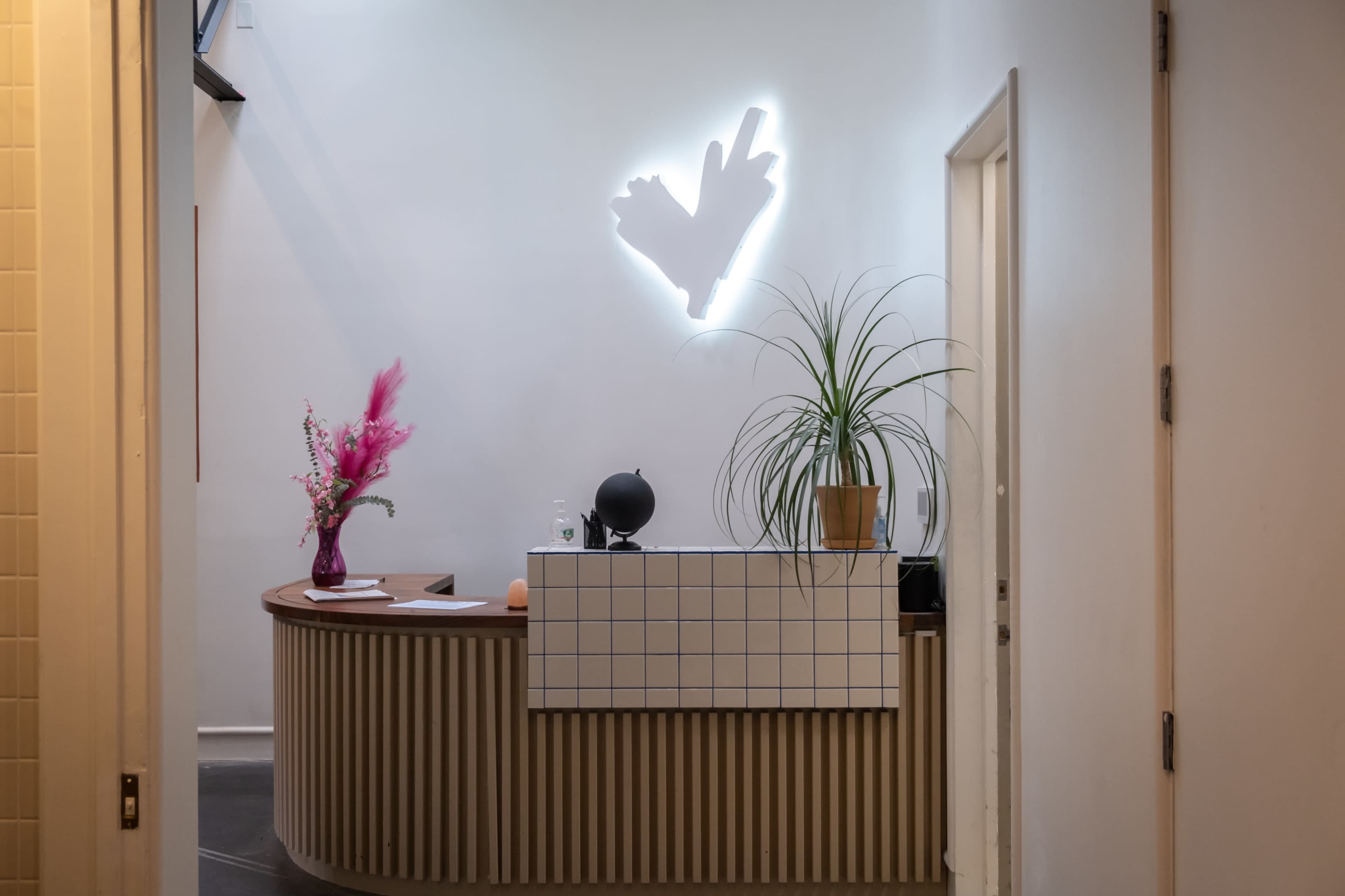 The image shows a modern reception desk adorned with a potted plant, a decorative vase with flowers, and a light fixture on the wall behind it.