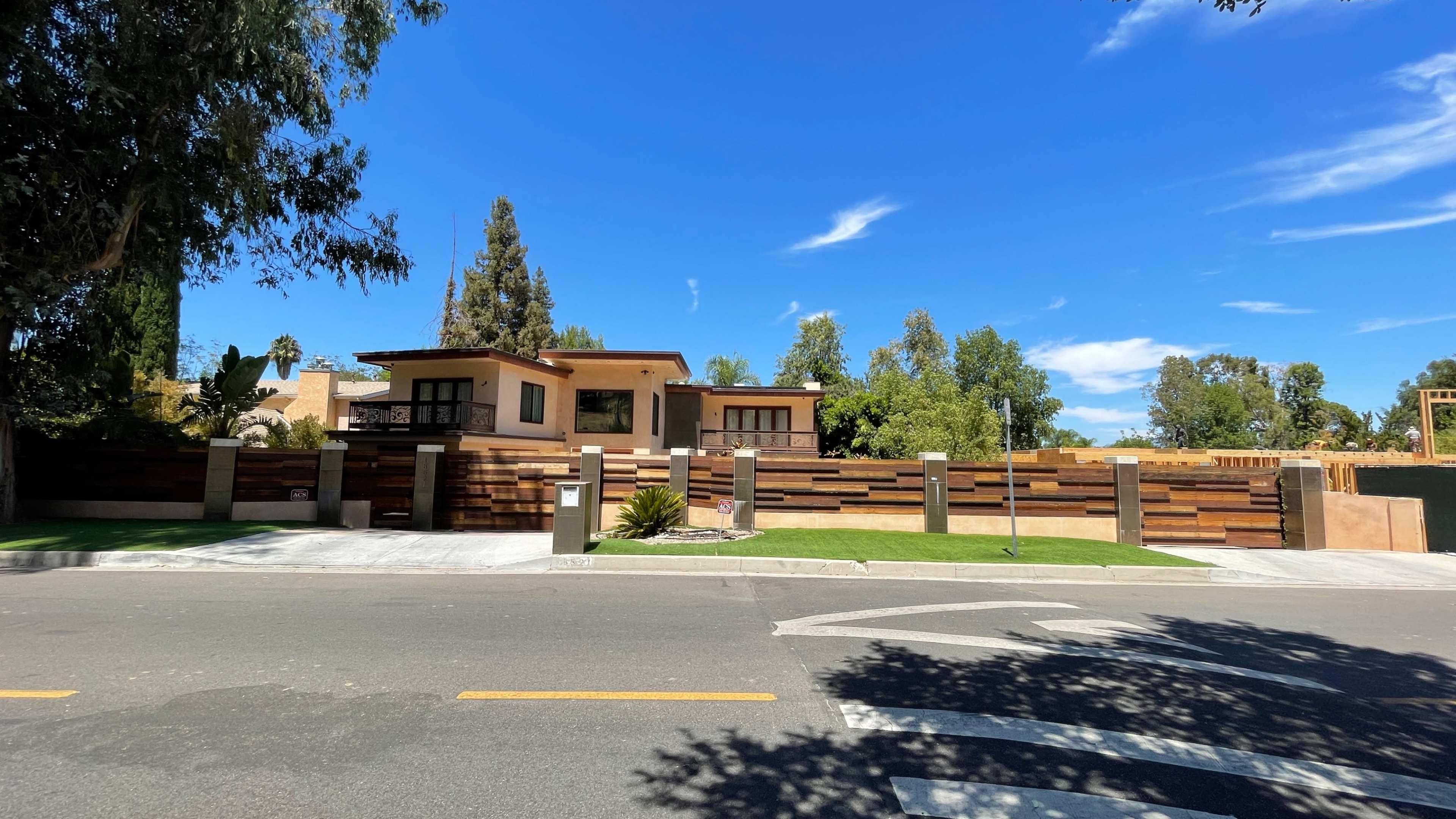 A modern house with a wooden fence and landscaped yard is visible from the street under a clear blue sky.