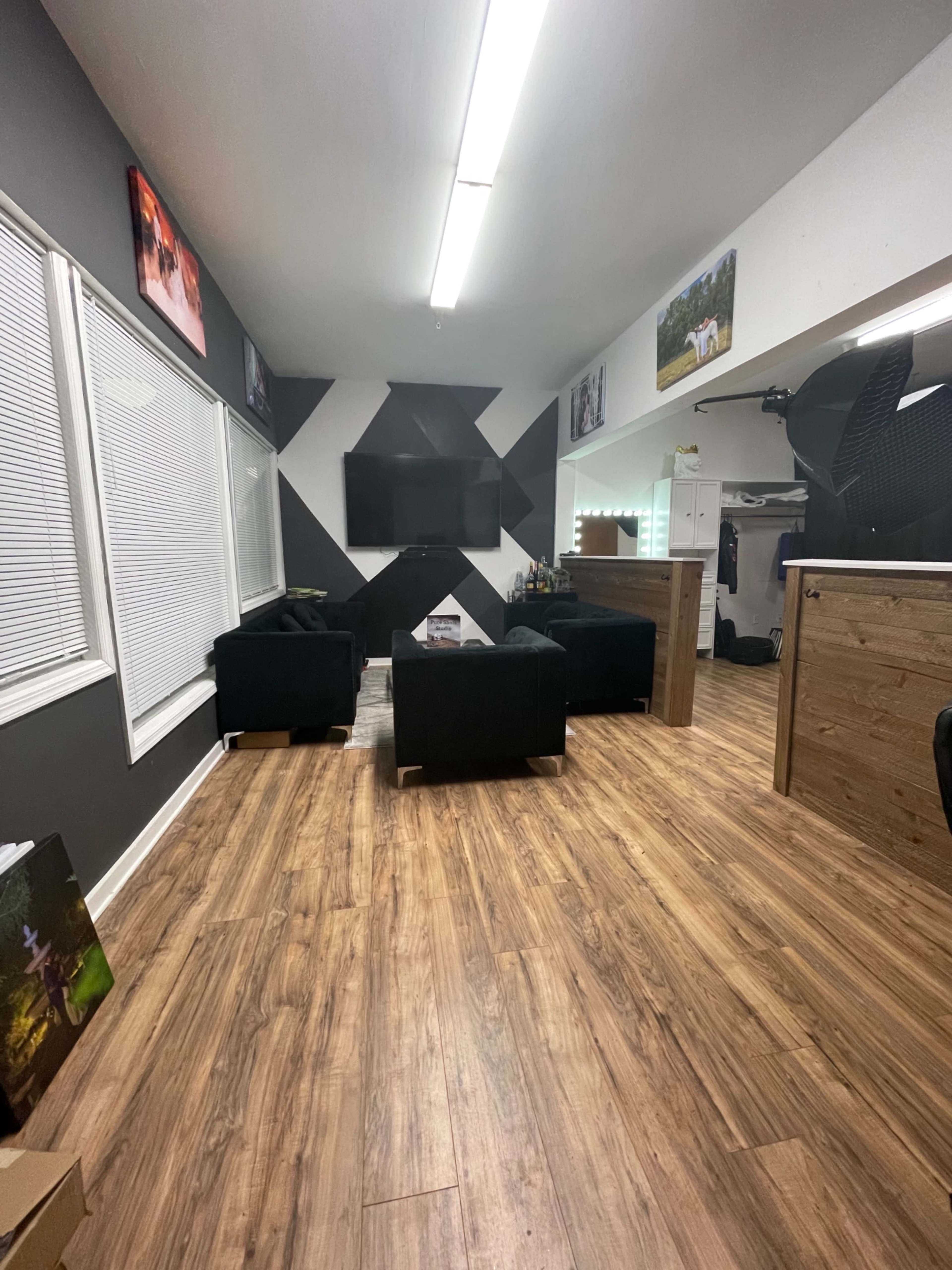 A modern lounge area with dark furniture, a large television on a geometric black and white wall, and wooden flooring.