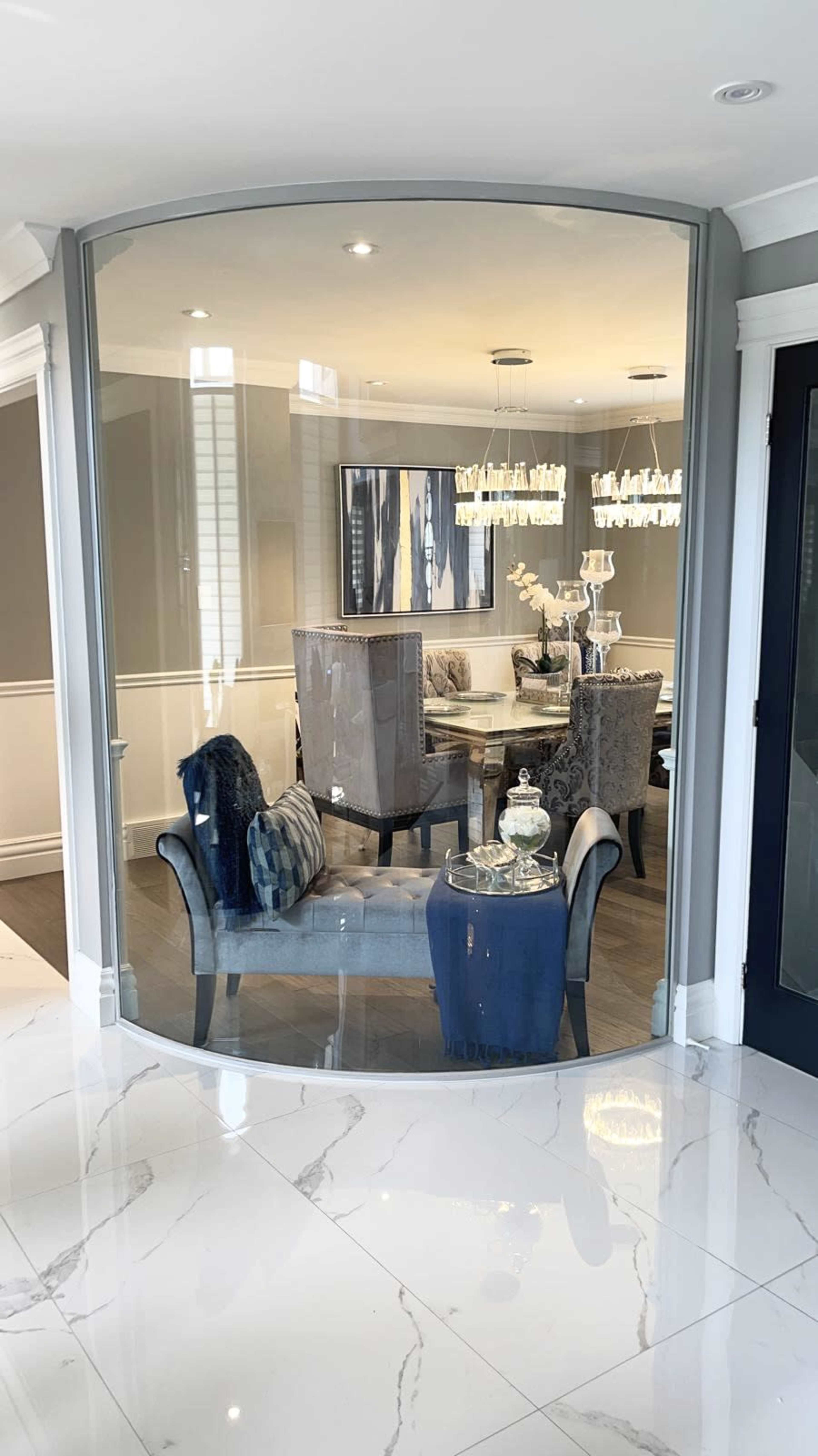 A modern living space is reflected in a curved glass partition, showcasing a dining area with stylish furniture and decorative lighting.