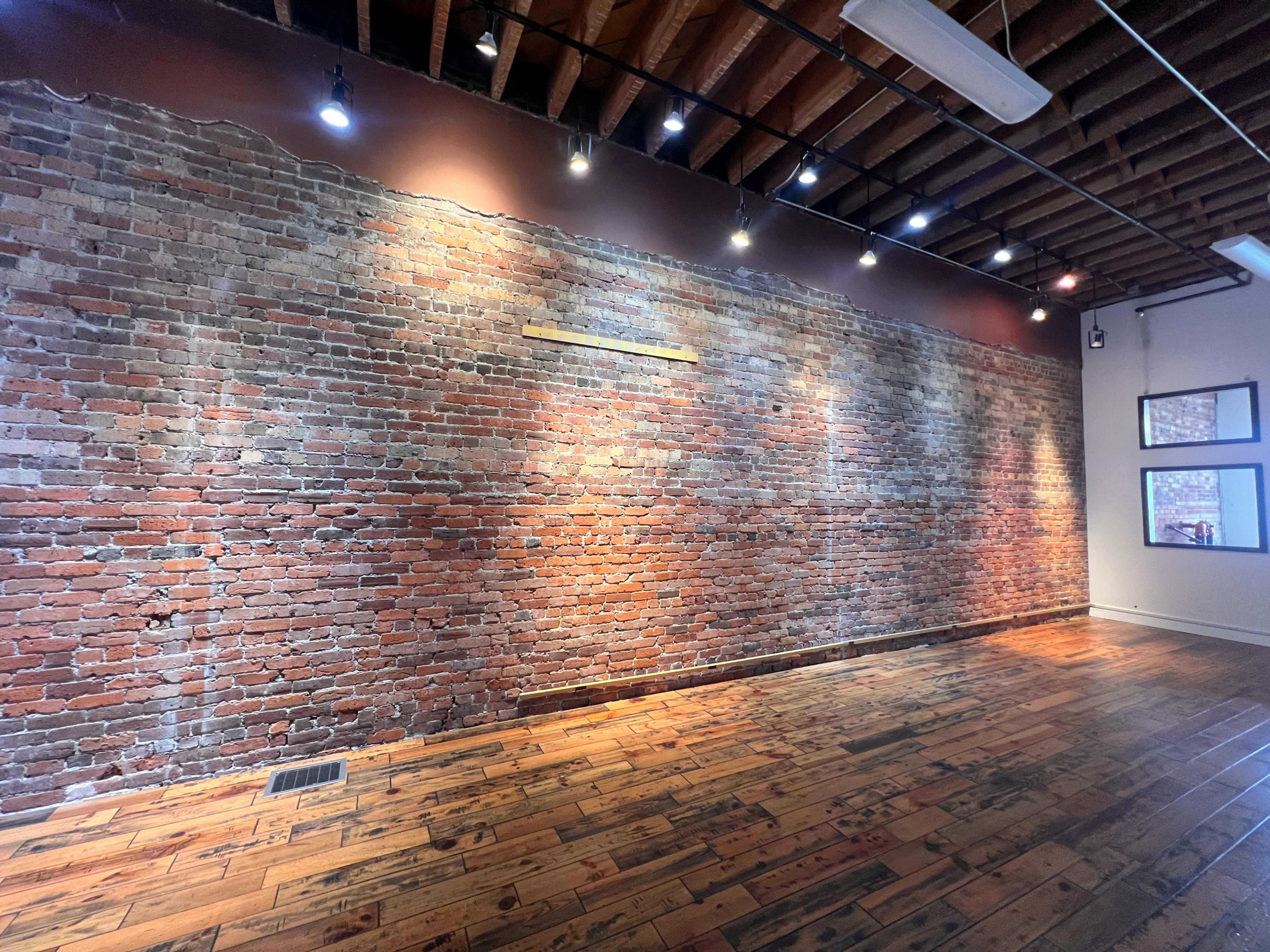 The image shows a brick wall with evenly spaced lighting, complemented by wooden flooring in a spacious room.