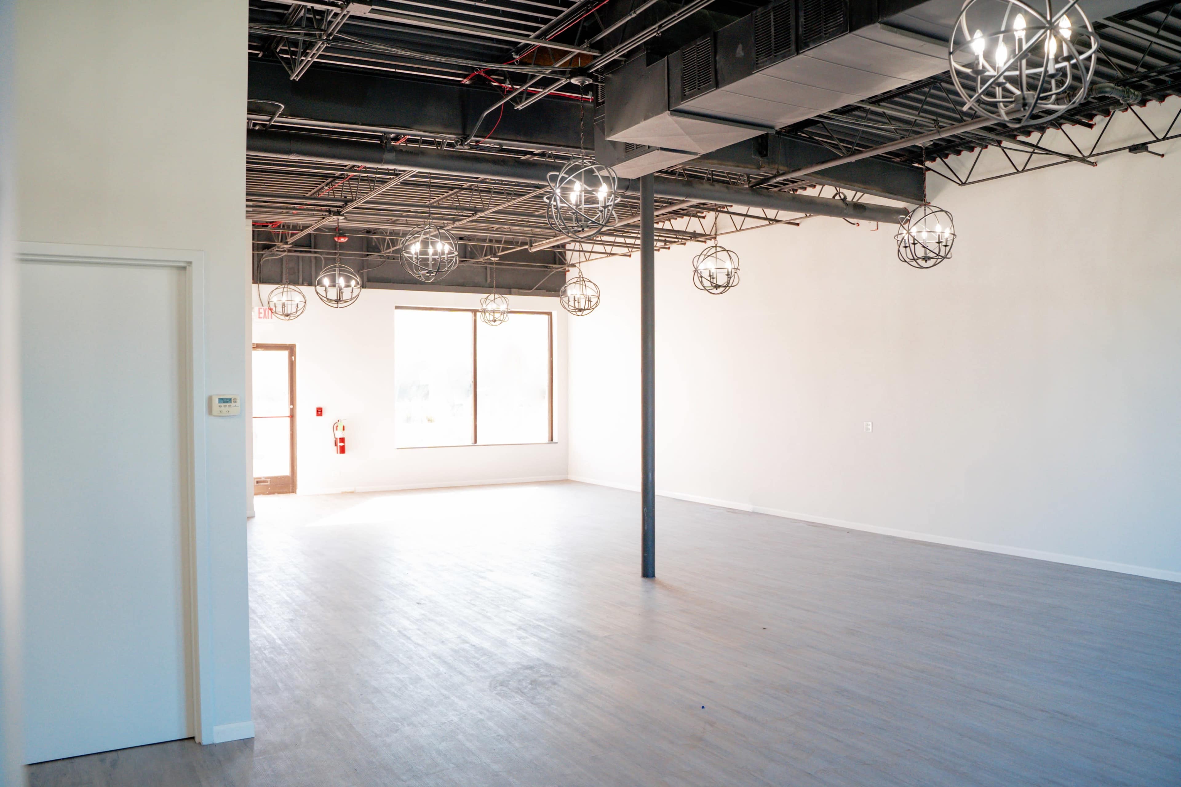 An empty commercial space with modern lighting fixtures and large windows illuminating light-colored wooden flooring.